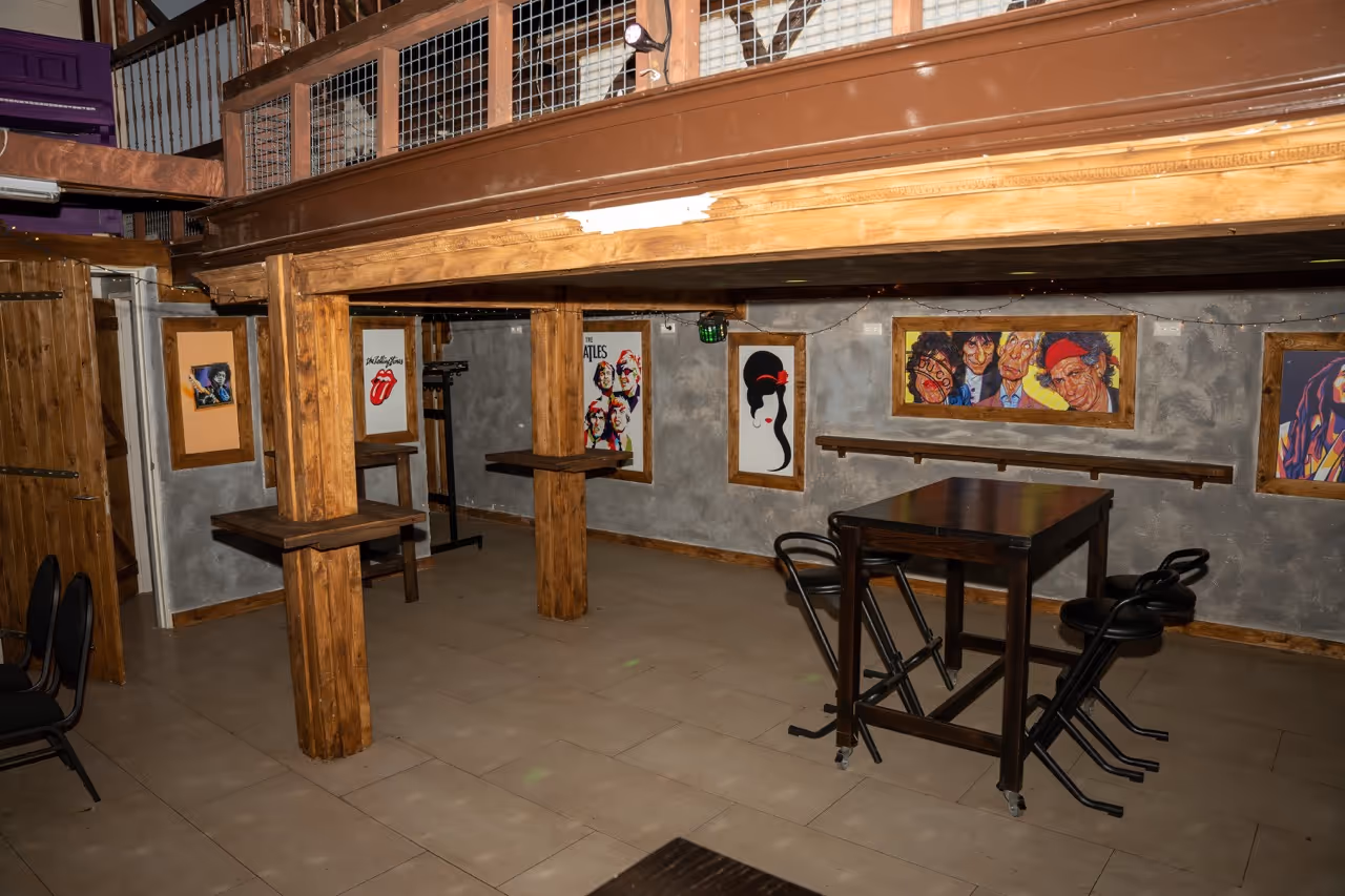 Interieur van een café met houten balken, een hoge tafel met zwarte krukken en muurschilderijen van muzikanten zoals The Rolling Stones en The Beatles.