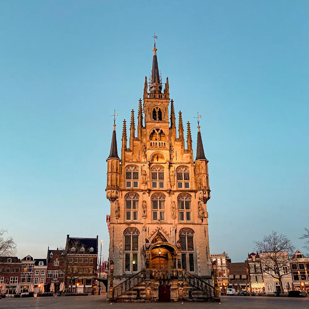 Historisch gotisch stadshuis met spitsen en decoratieve beelden aan een plein bij zonsondergang.