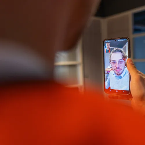 Persoon voert videogesprek op smartphone met een man met bril en lichte trui.