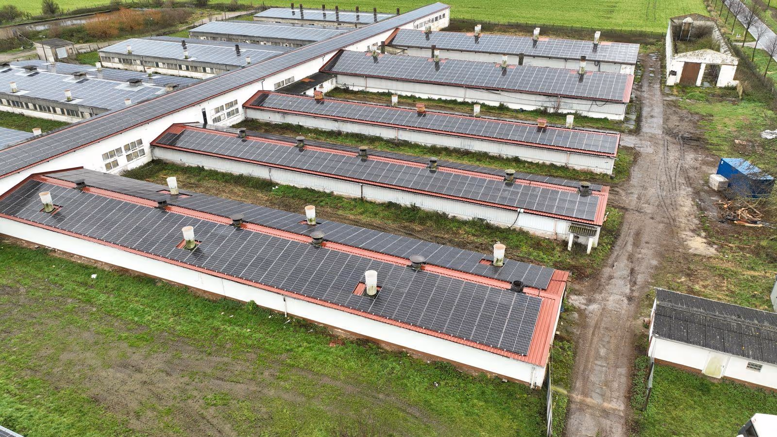 Gebäudekomplex mit vielen Solarzellen auf den Dächern, umgeben von Grünflächen und Schotterwegen.