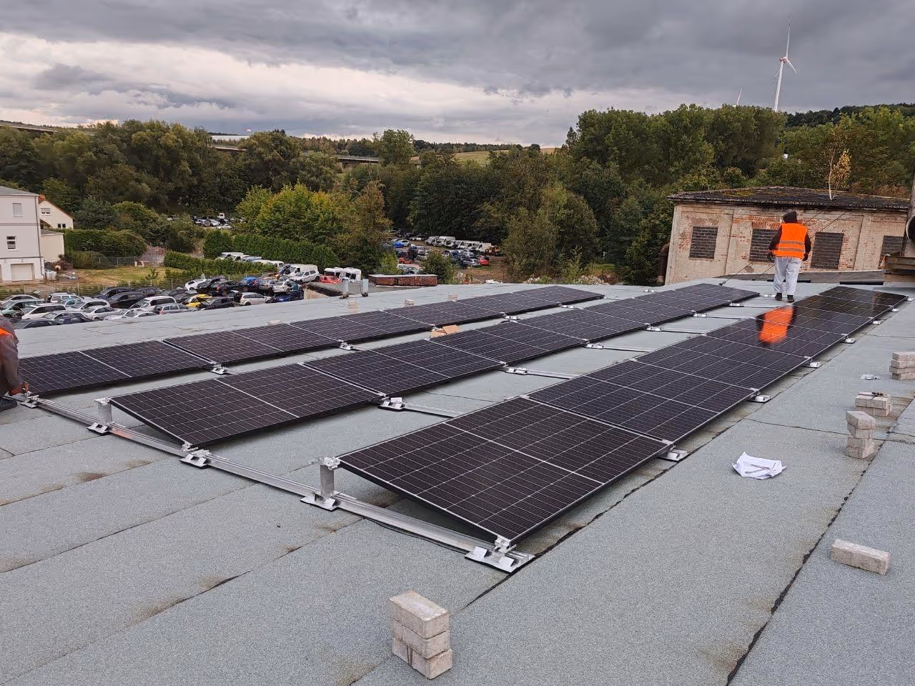 Installation von Solarpanels auf einem flachen Dach mit einer Person in orangefarbener Sicherheitsweste.