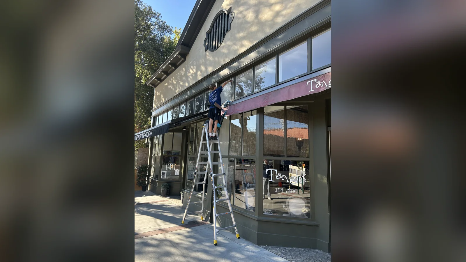 Technician on a ladder cleaning storefront windows