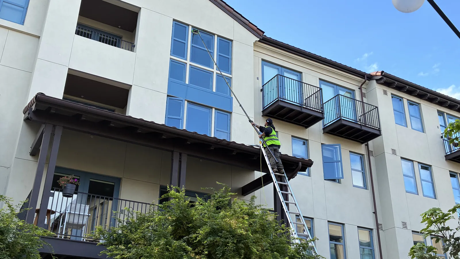Technician on a ladder cleaning windows on a multifamily building