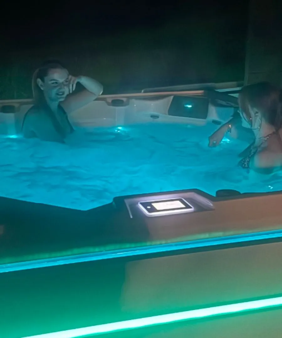 Zwei Personen entspannen in einem blau beleuchteten Whirlpool bei Nacht