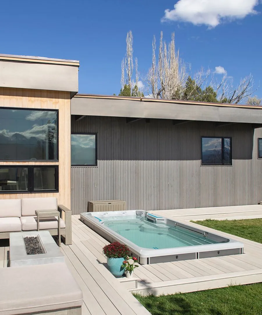 Moderner Swimmingpool auf einer Holzterrasse mit Feuerstelle und kahlen Bäumen