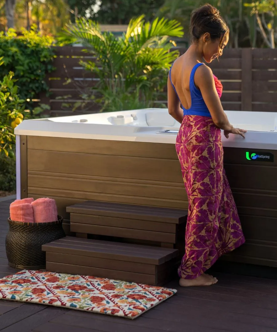 Frau im blauen Top und gemusterten Rock steht neben Whirlpool im Garten