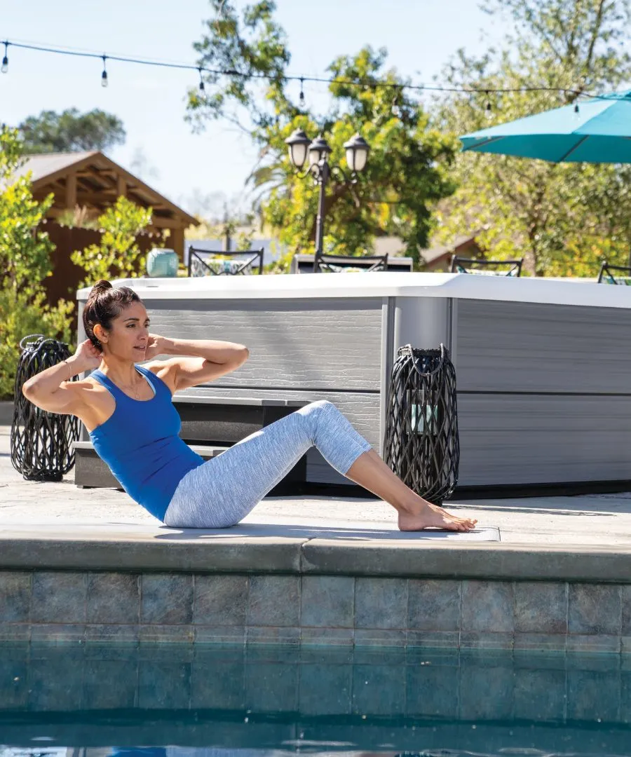 Frau macht Yoga-Übung neben Pool im Freien mit Sonnenschirm im Hintergrund