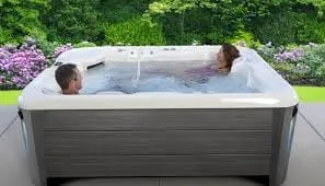 Zwei Personen entspannen in einem Außen-Whirlpool mit Blumenbeeten im Hintergrund