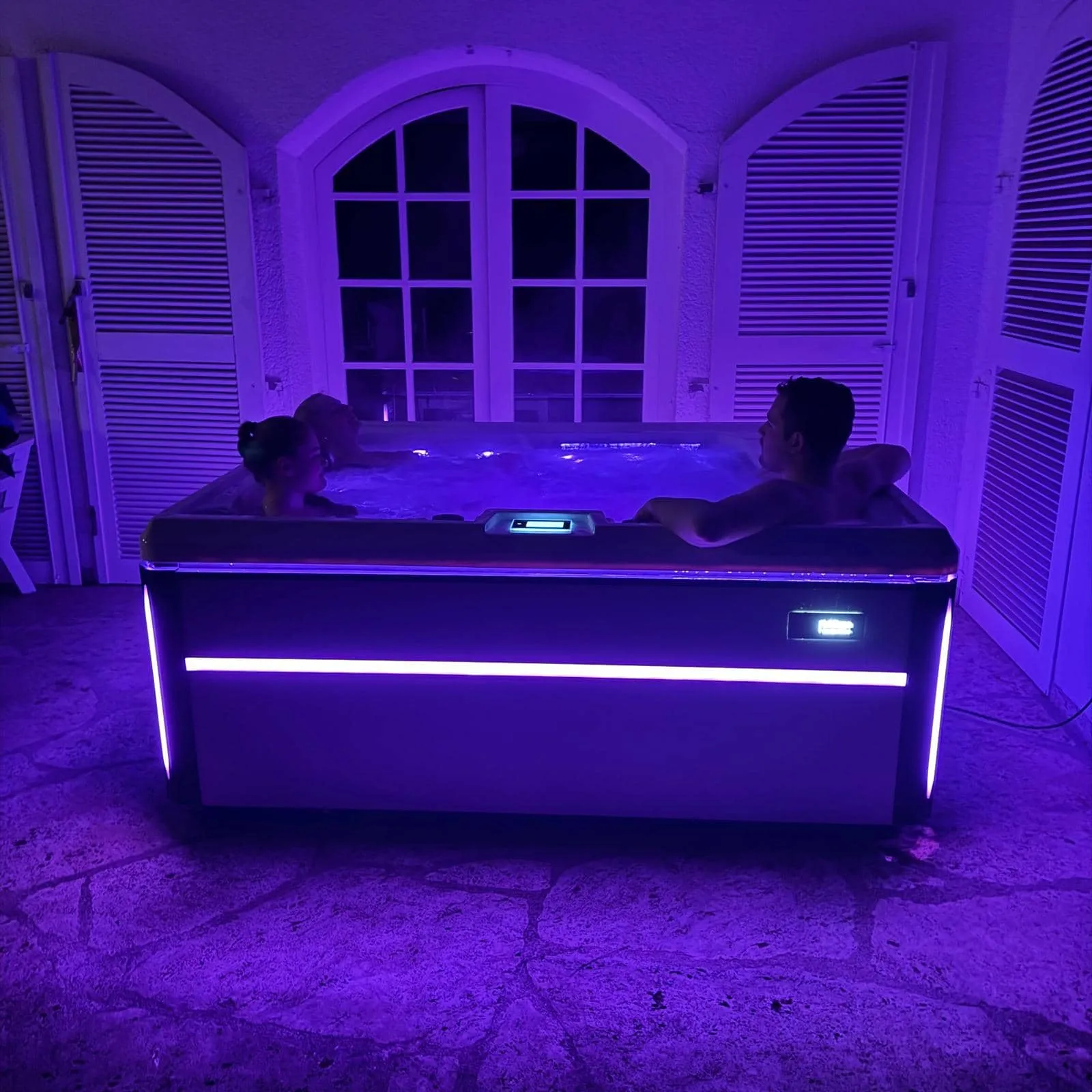 Zwei Personen entspannen im beleuchteten Whirlpool mit lila Ambiente