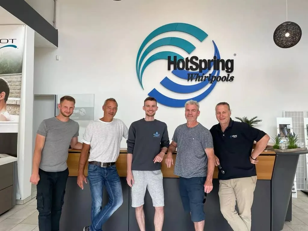Fünf Männer vor dem HotSpring Whirlpools Logo im Büro