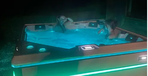 Das Bild zeigt zwei Personen, die sich bei Nacht in einem stilvoll beleuchteten Whirlpool entspannen. Die sanfte blaue Beleuchtung und die gemütliche Atmosphäre vermitteln ein Gefühl von Ruhe und Erholung.