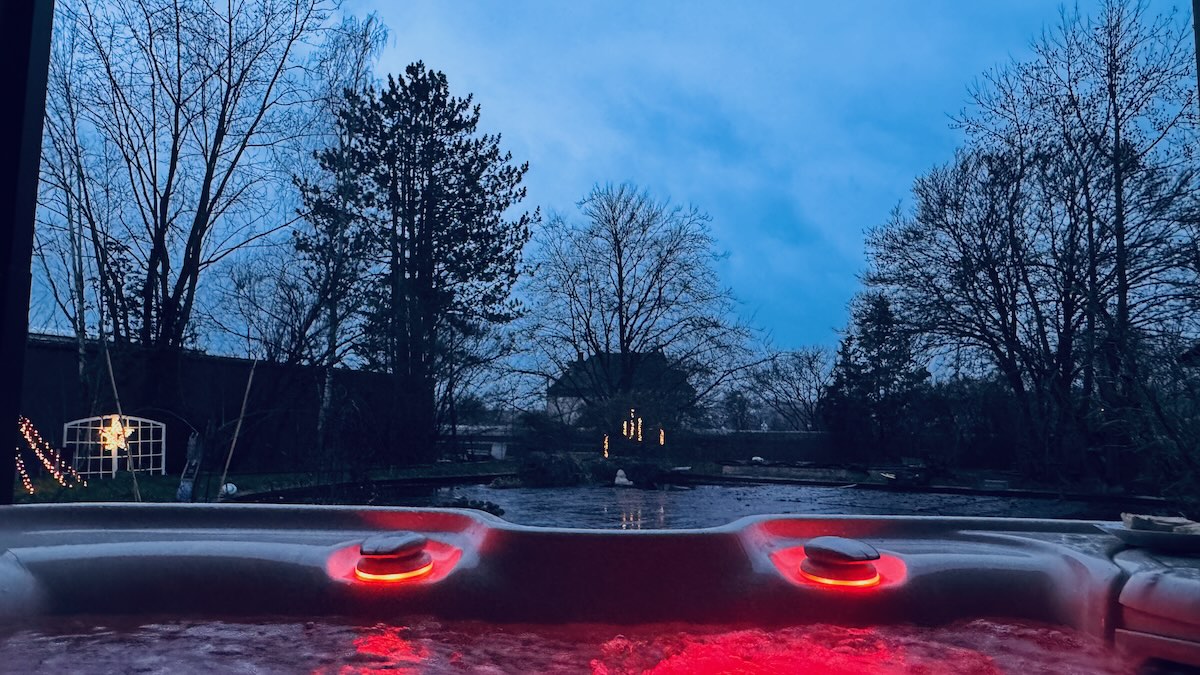 Neujahrgruß von spaPRO: Sicht aus spaPRO Whirlpool im dunklen Garten mit roter LED-Beleuchtung.