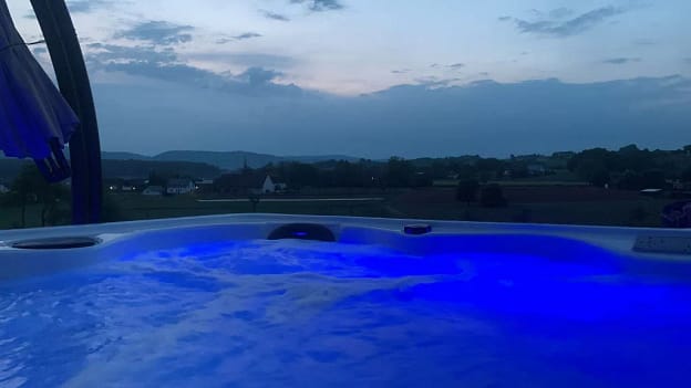 Beleuchteter Whirlpool eines spaPRO-Kunden mit Blick auf die Landschaft in der Abenddämmerung