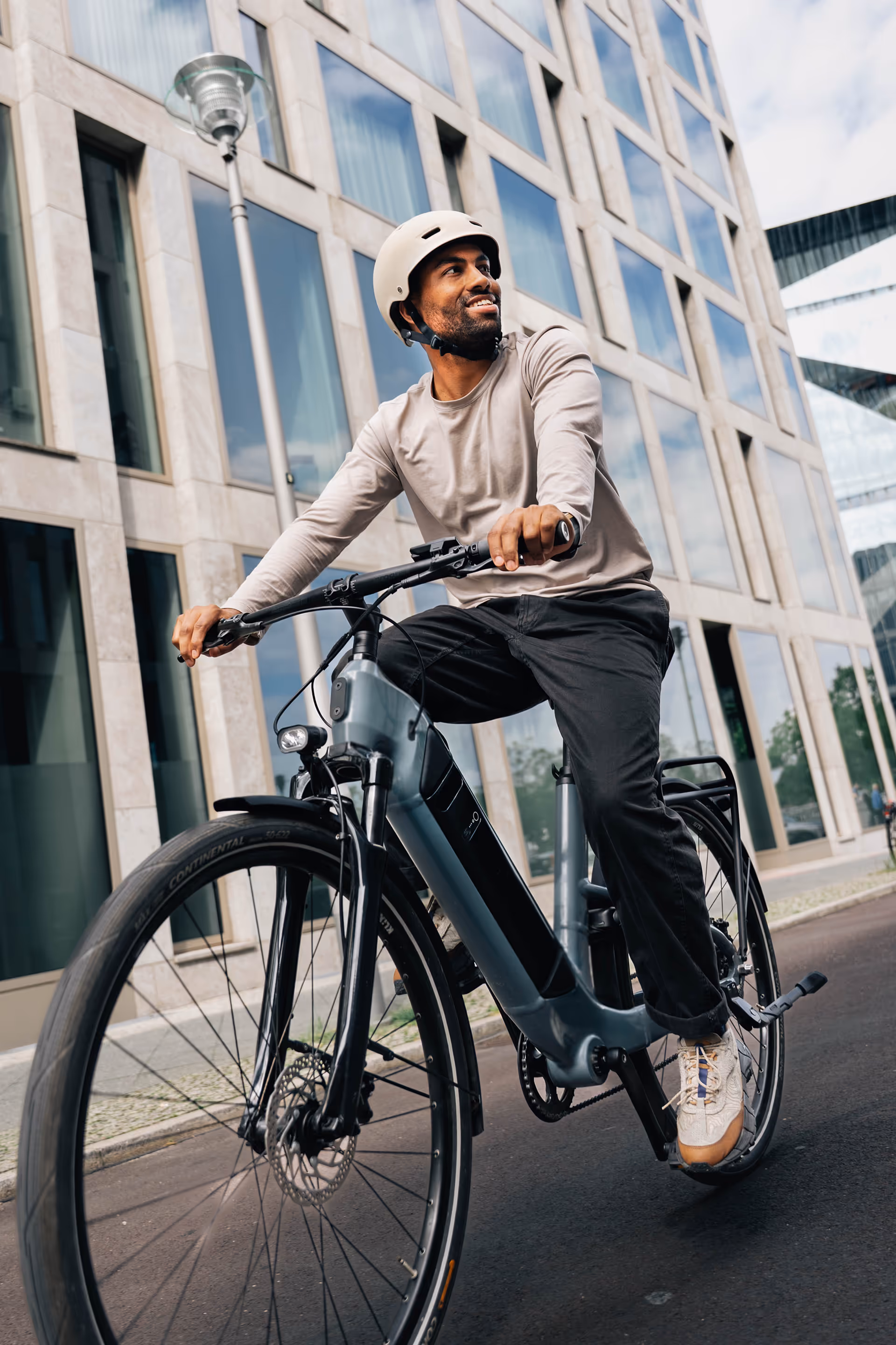 Man wearing a helmet riding an electric bicycle on an urban street with modern buildings.