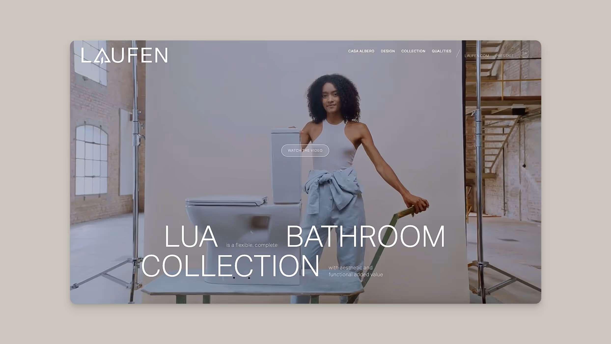 Woman with curly hair pushes a wheelbarrow carrying bathroom fixtures against a light backdrop in an industrial-style room.