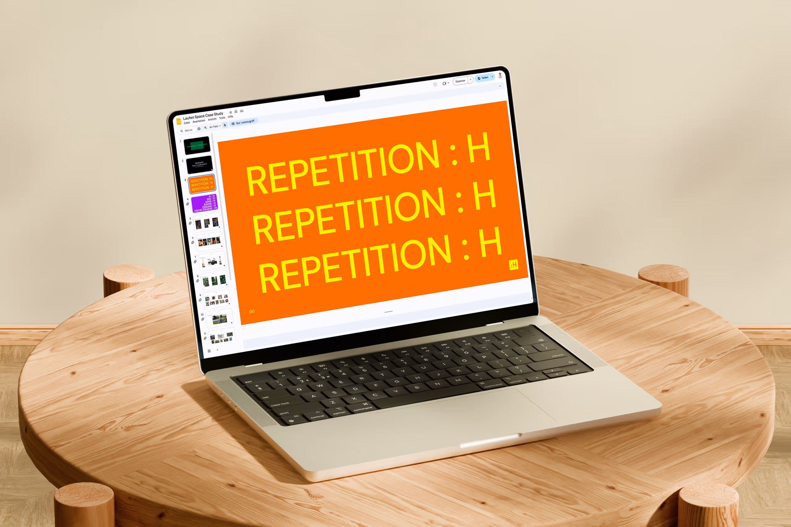 Laptop on round wooden table displaying a presentation slide with large yellow text repeating 'REPETITION : H' on an orange background.