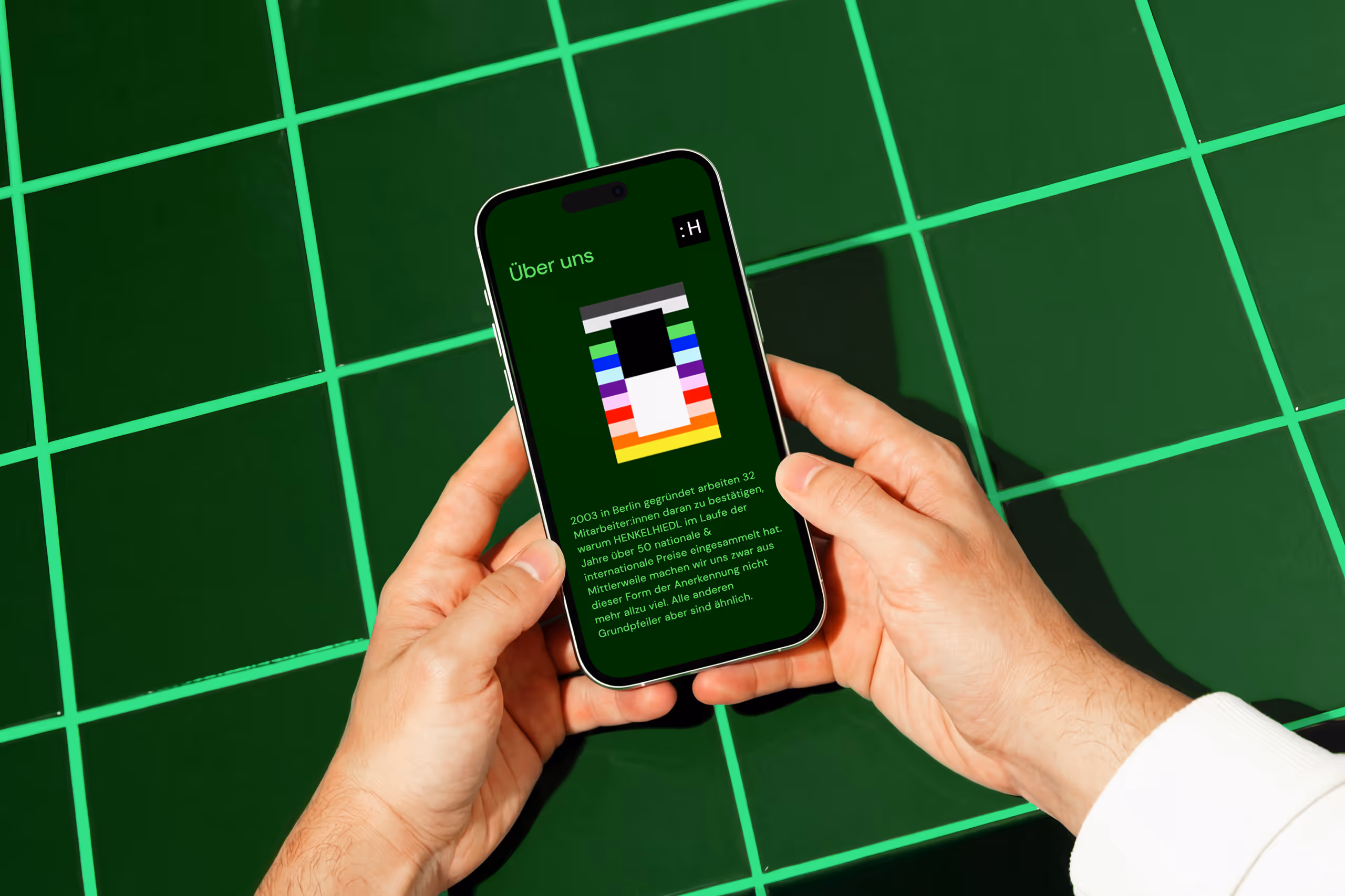 Person holding a smartphone displaying a green screen with colorful rectangular graphic and German text about a Berlin-based company.