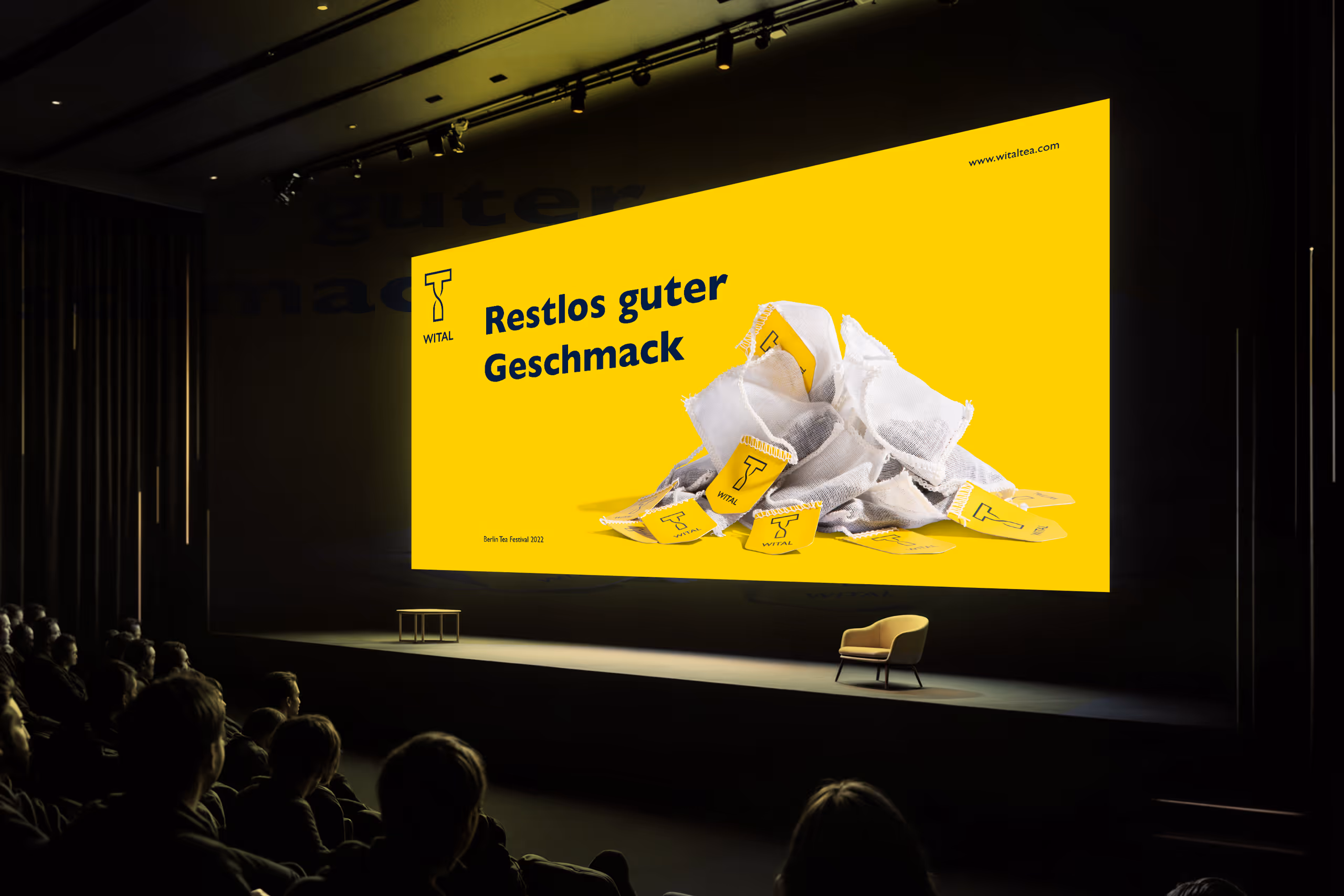 Audience watching a presentation with a bright yellow slide displaying a pile of tea bags and the text 'Restlos guter Geschmack' in German.