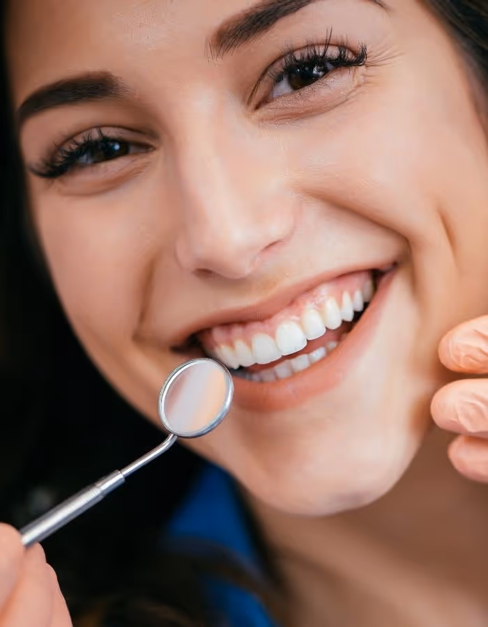 Close-up of a smiling woman showing her teeth during a dental checkup with a dental mirror.