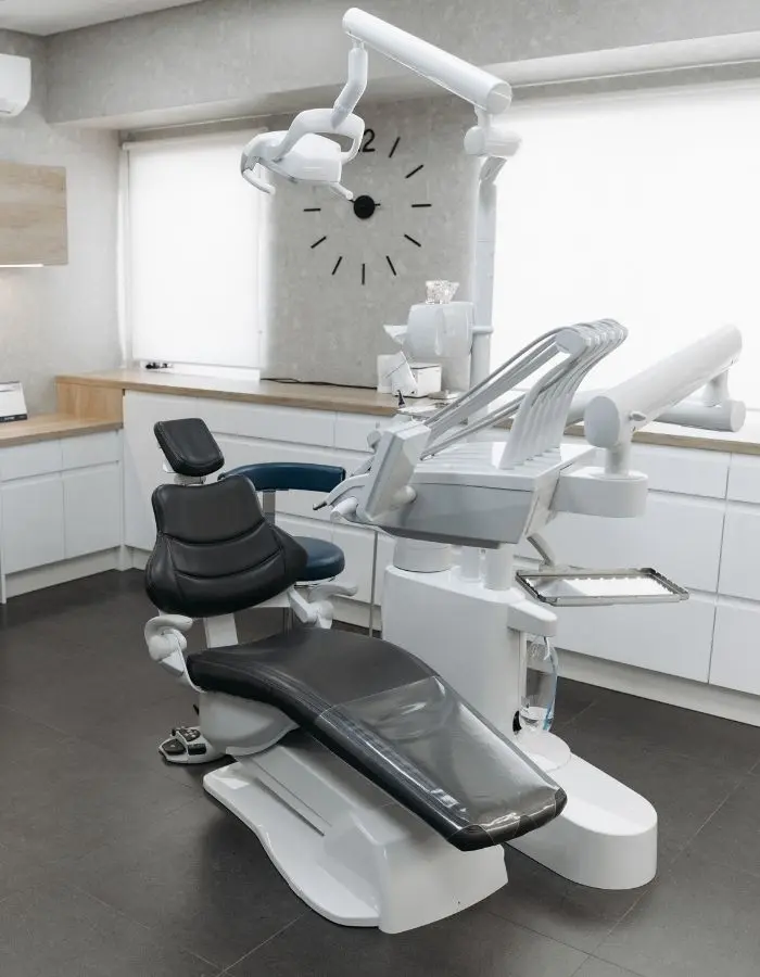 Modern dental examination room featuring a black dental chair with attached equipment and a wall clock in a bright, clean space.