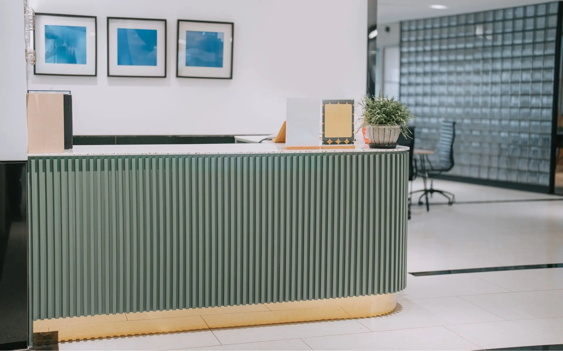 Modern reception desk with green vertical paneling, decorative frames on the wall, and an office chair in the background.