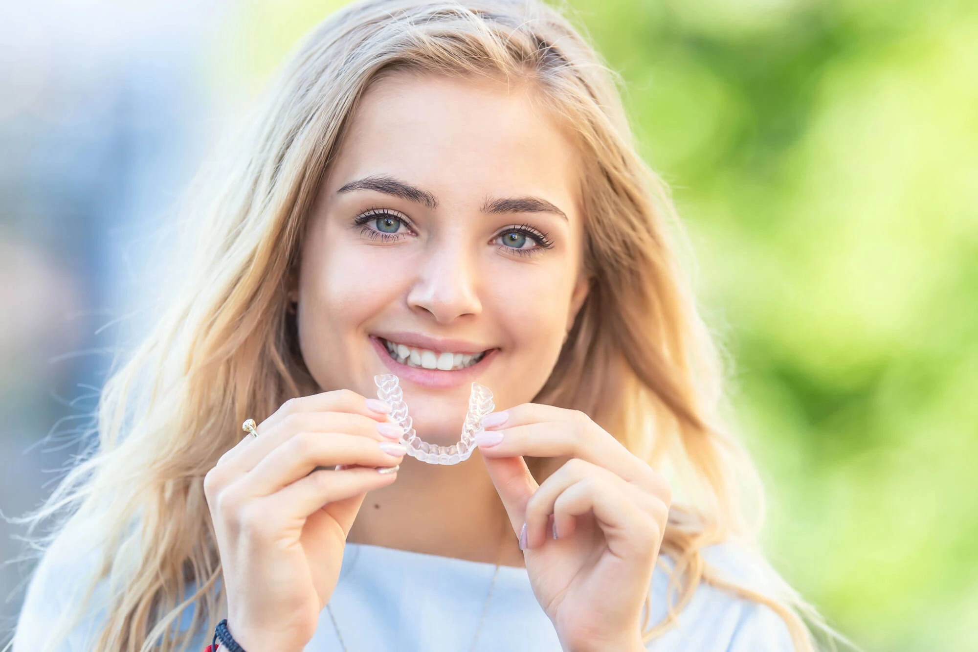 Smiling woman holding a clear dental aligner in front of her teeth in Davie, FL
