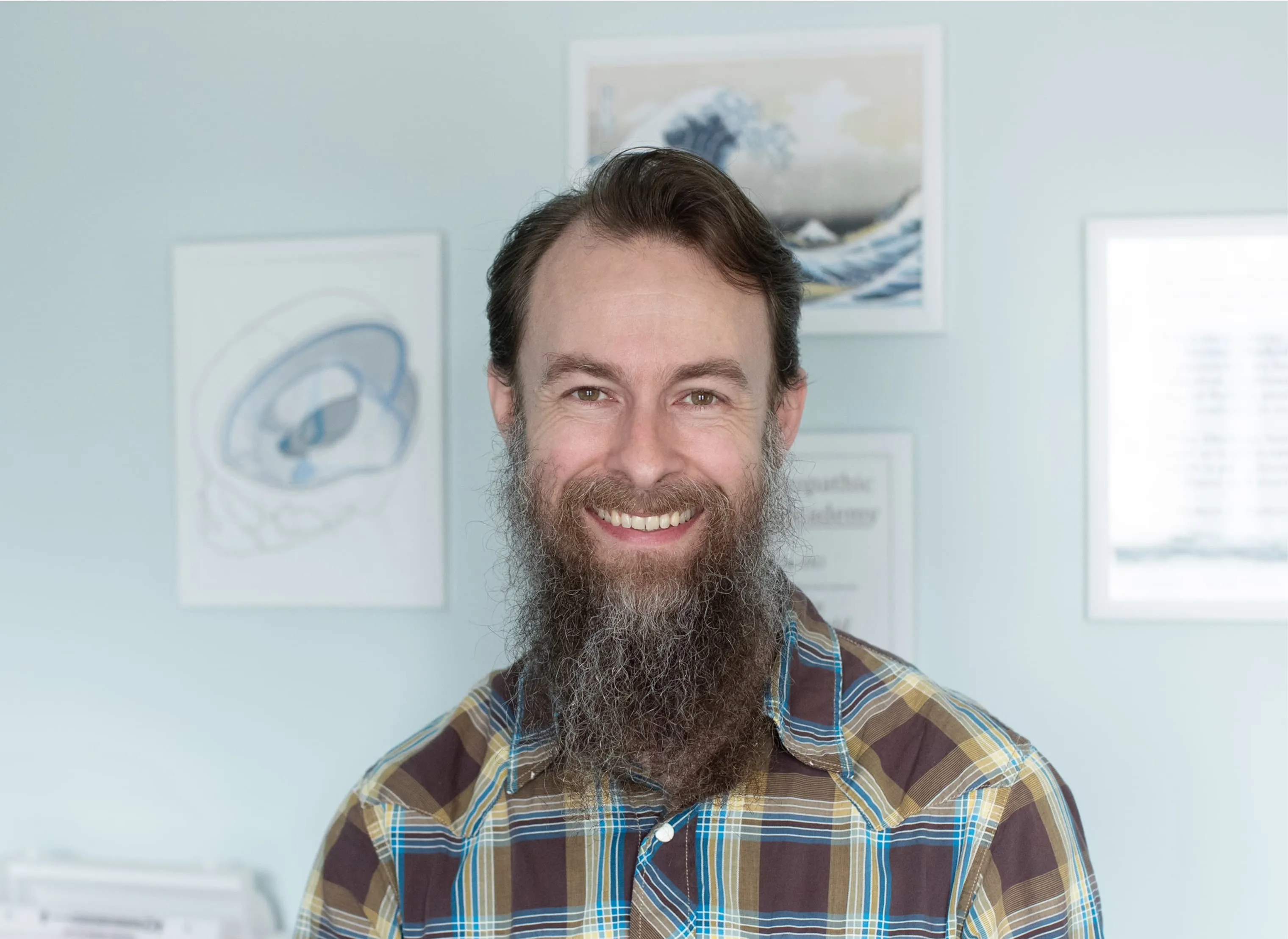 Headshot portrait of Dr. Joseph McCue smiling, wearing a plaid button-down shirt