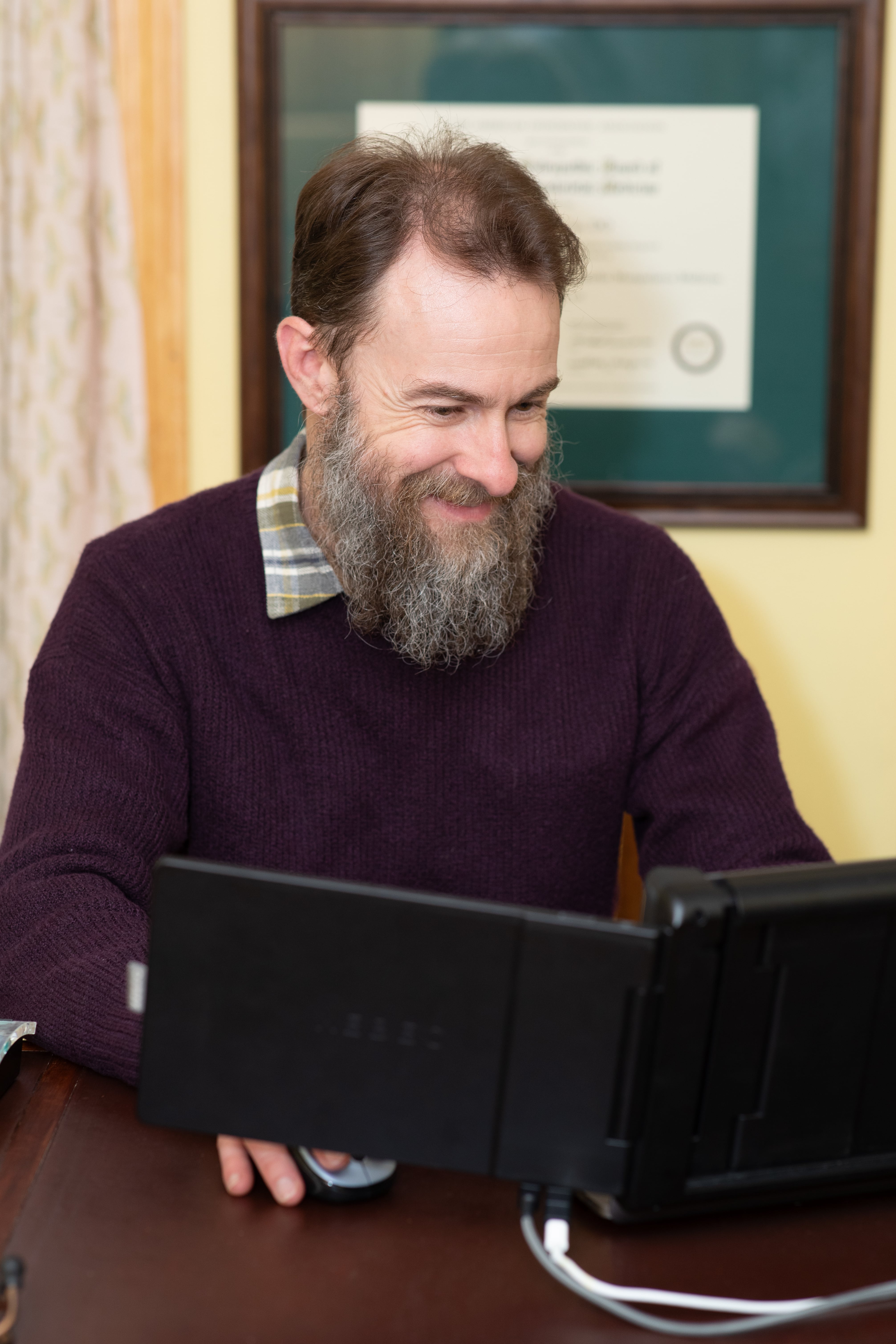 Dr. Joseph McCue smiling while reviewing patient records at his desk, with a medical board certification displayed on the wall