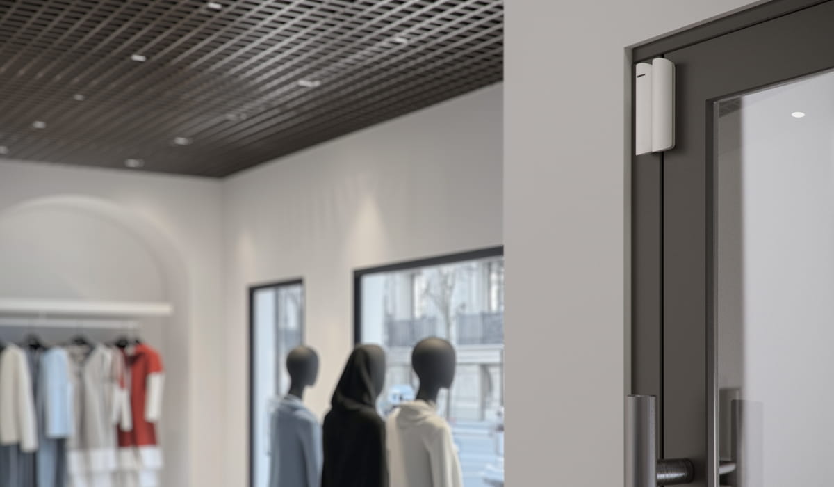 Ajax DoorProtect entry sensor installed on a commercial glass door in a retail store.