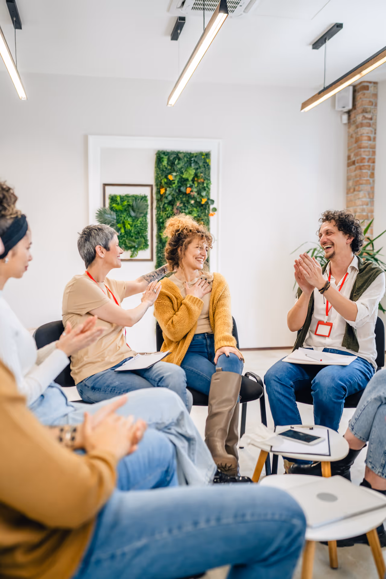 Group of people sitting in a circle indoors, smiling and clapping during a supportive therapy or group discussion session.