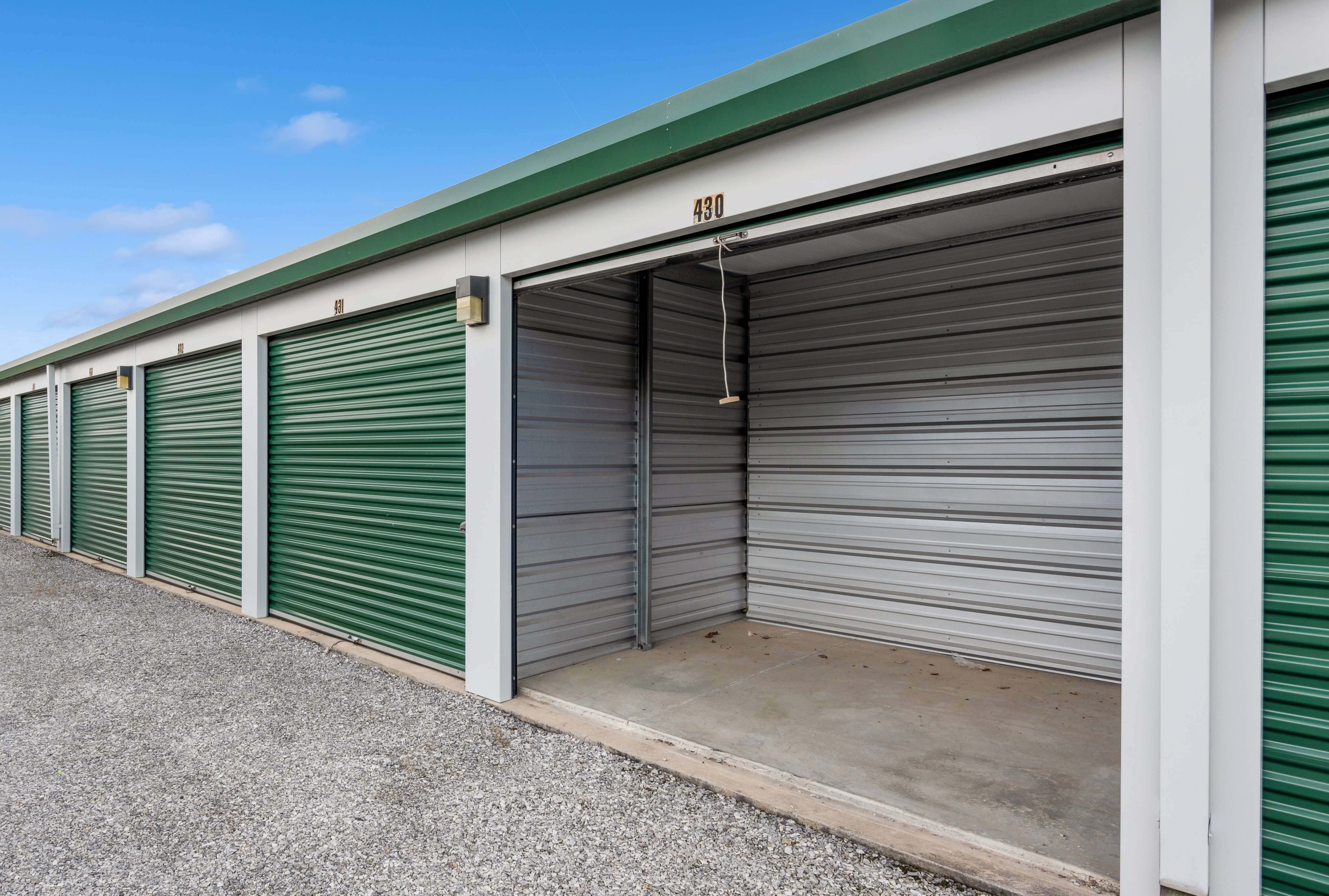 An open storage unit with a rolled-up metal door, showing a clean, well-lit interior space ready for storage. The concrete floor and metal walls demonstrate the unit's secure construction