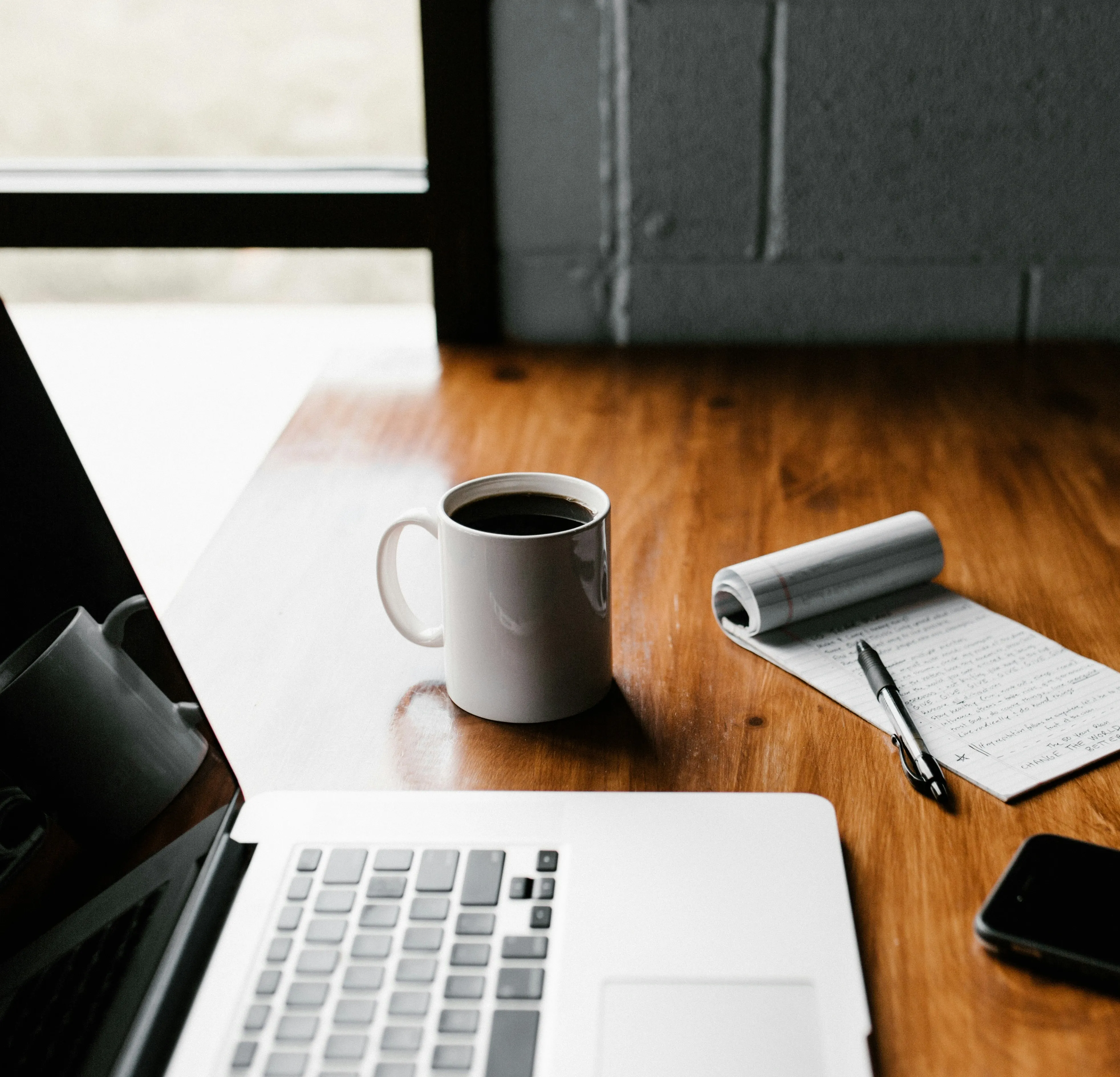 A laptop, a cup of coffe, and a note pad with a pencil over a desk