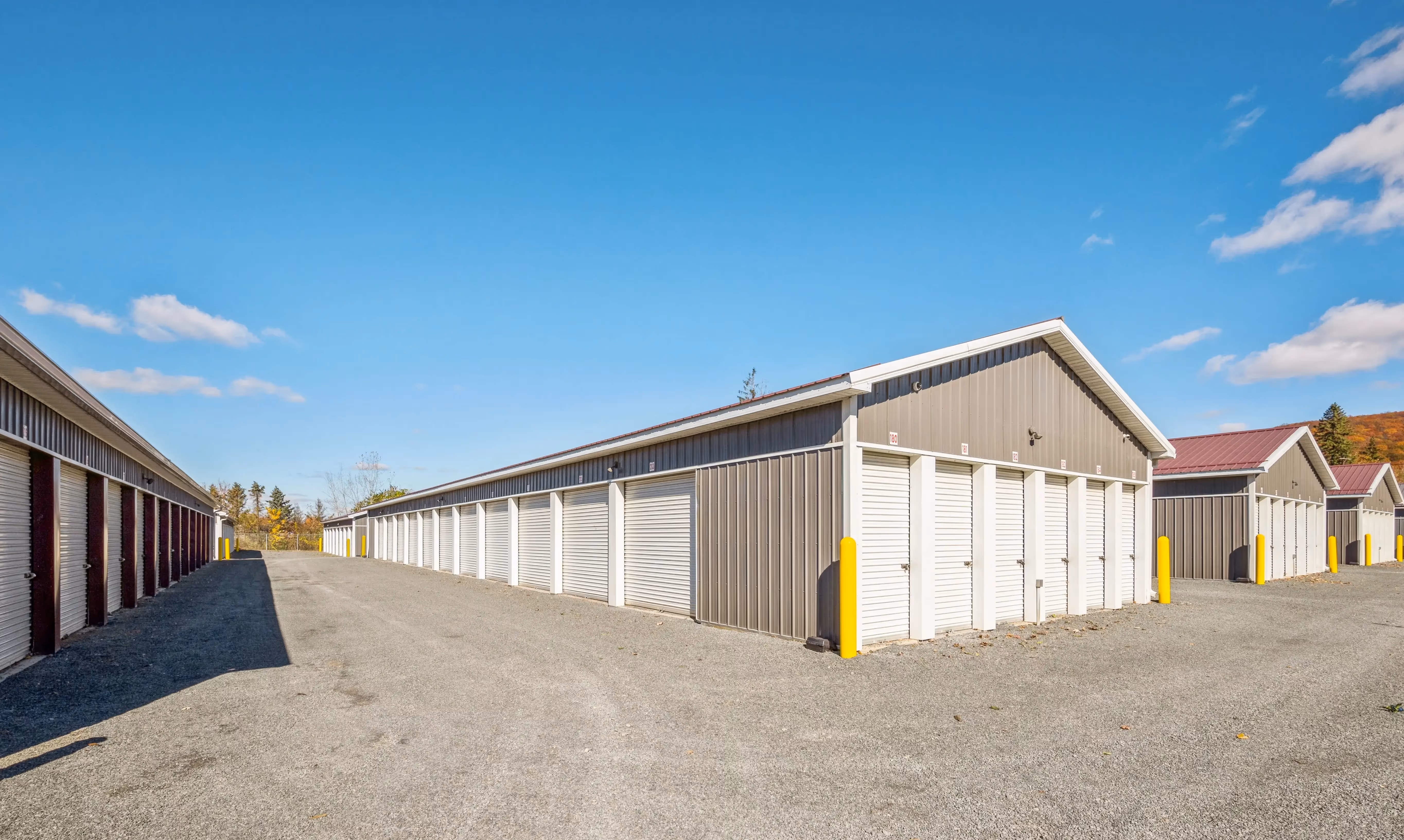 Drive up storage buildings with white doors and purple roofs along gravel access lanes in Elmira NY