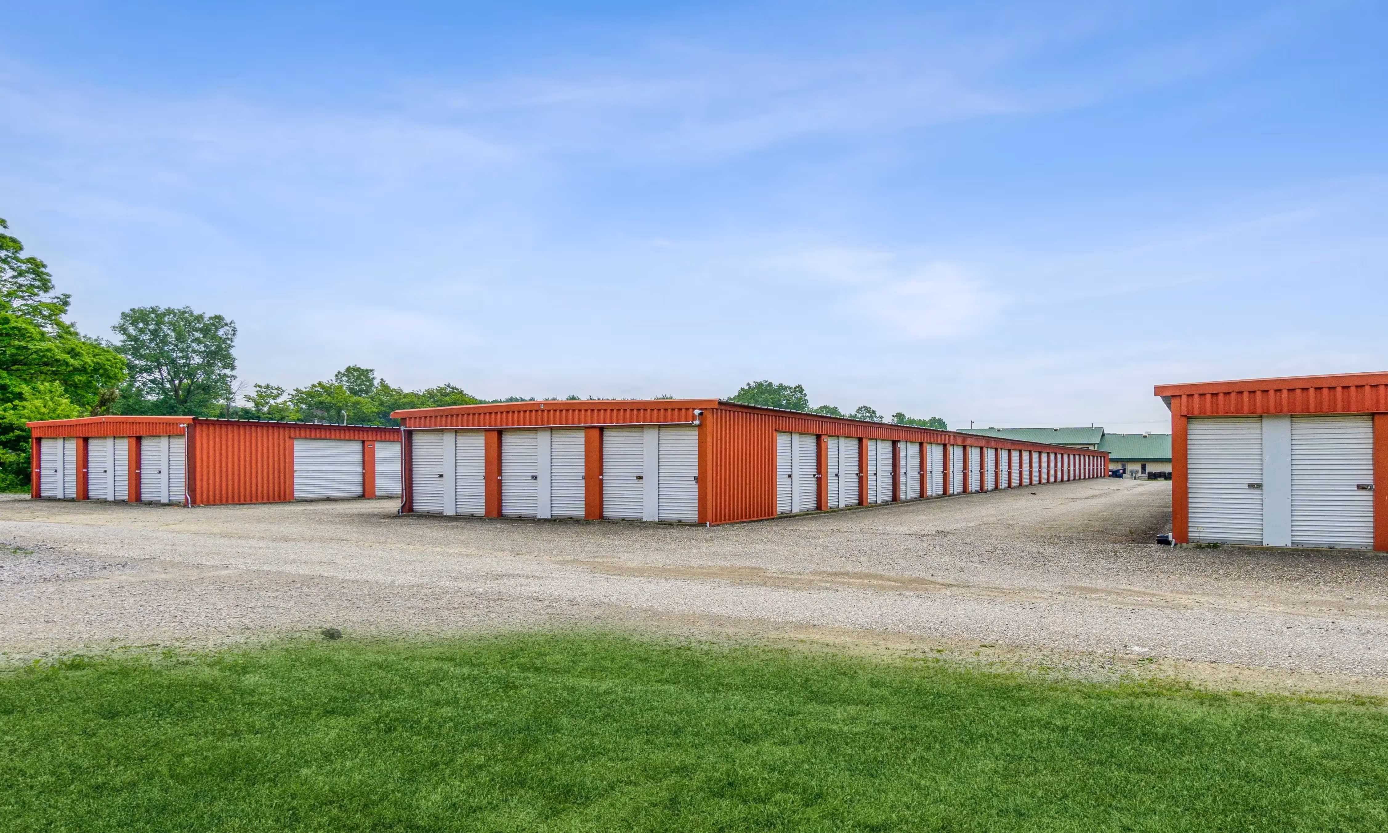 Drive up storage buildings with red walls and white doors bordered by a grassy area at our Fairview PA facility