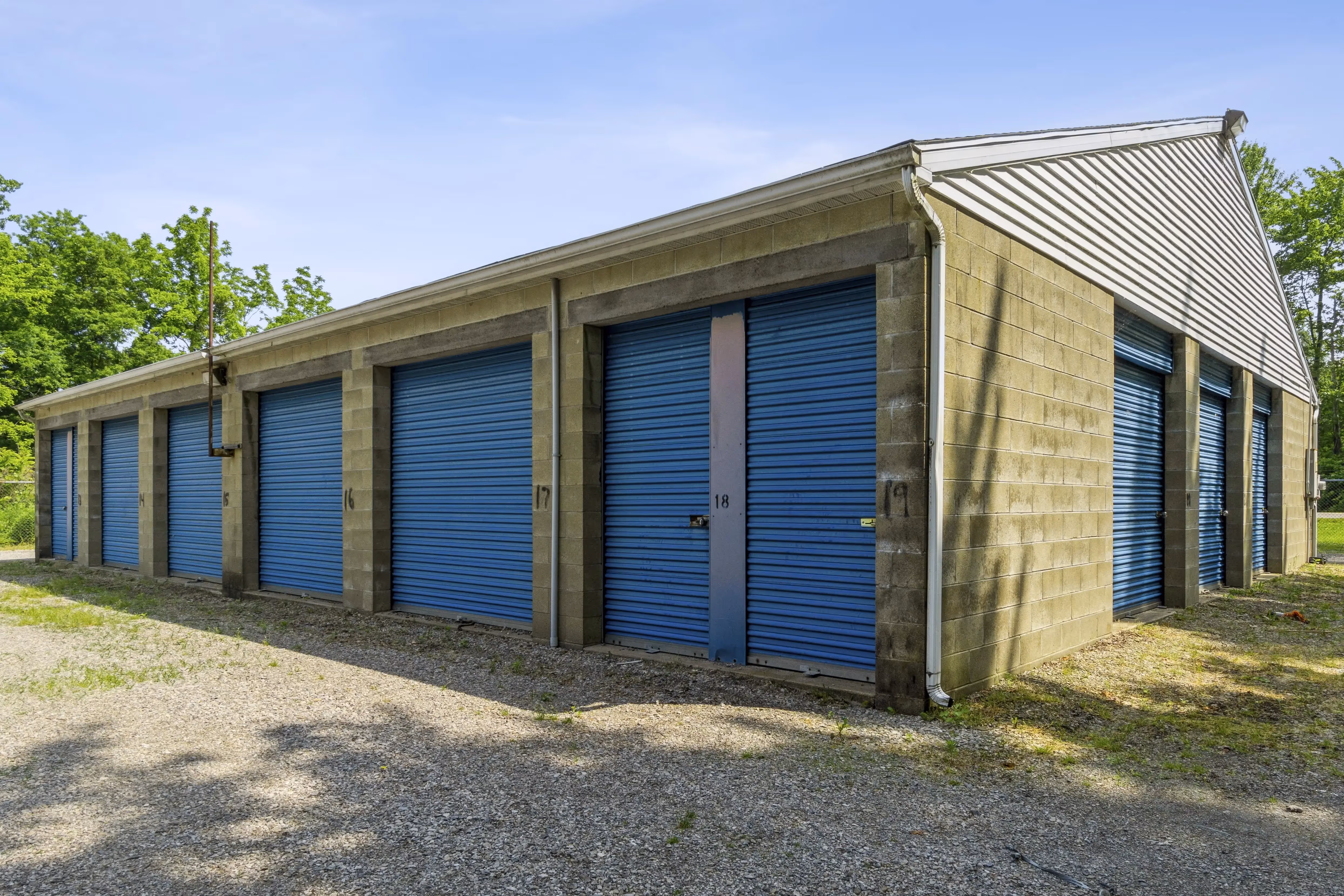 Angled view of storage units with blue roll up doors and gravel driveway in Fairview PA