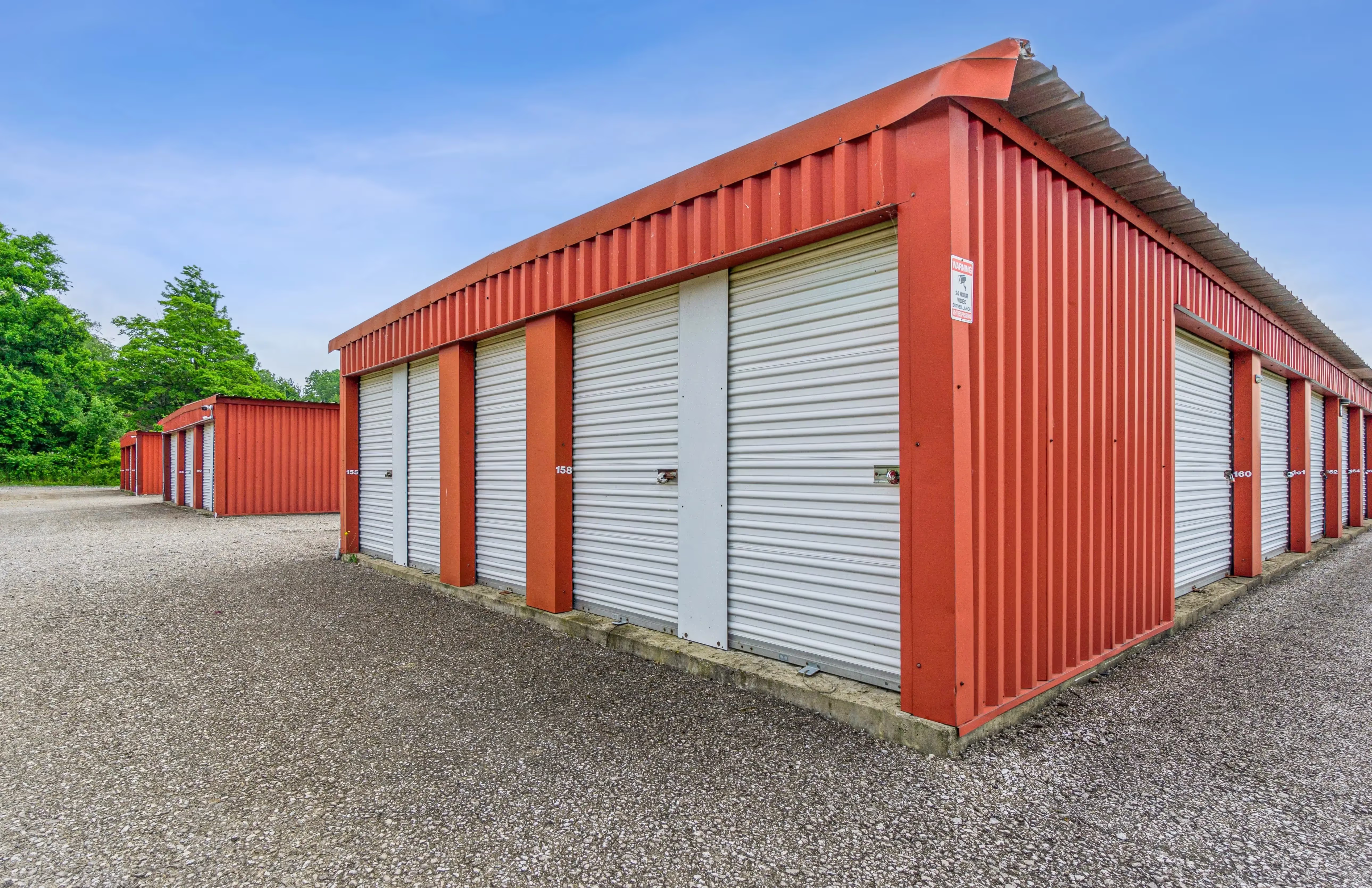 Corner perspective of red storage buildings with white roll up doors and gravel access area in Fairview PA