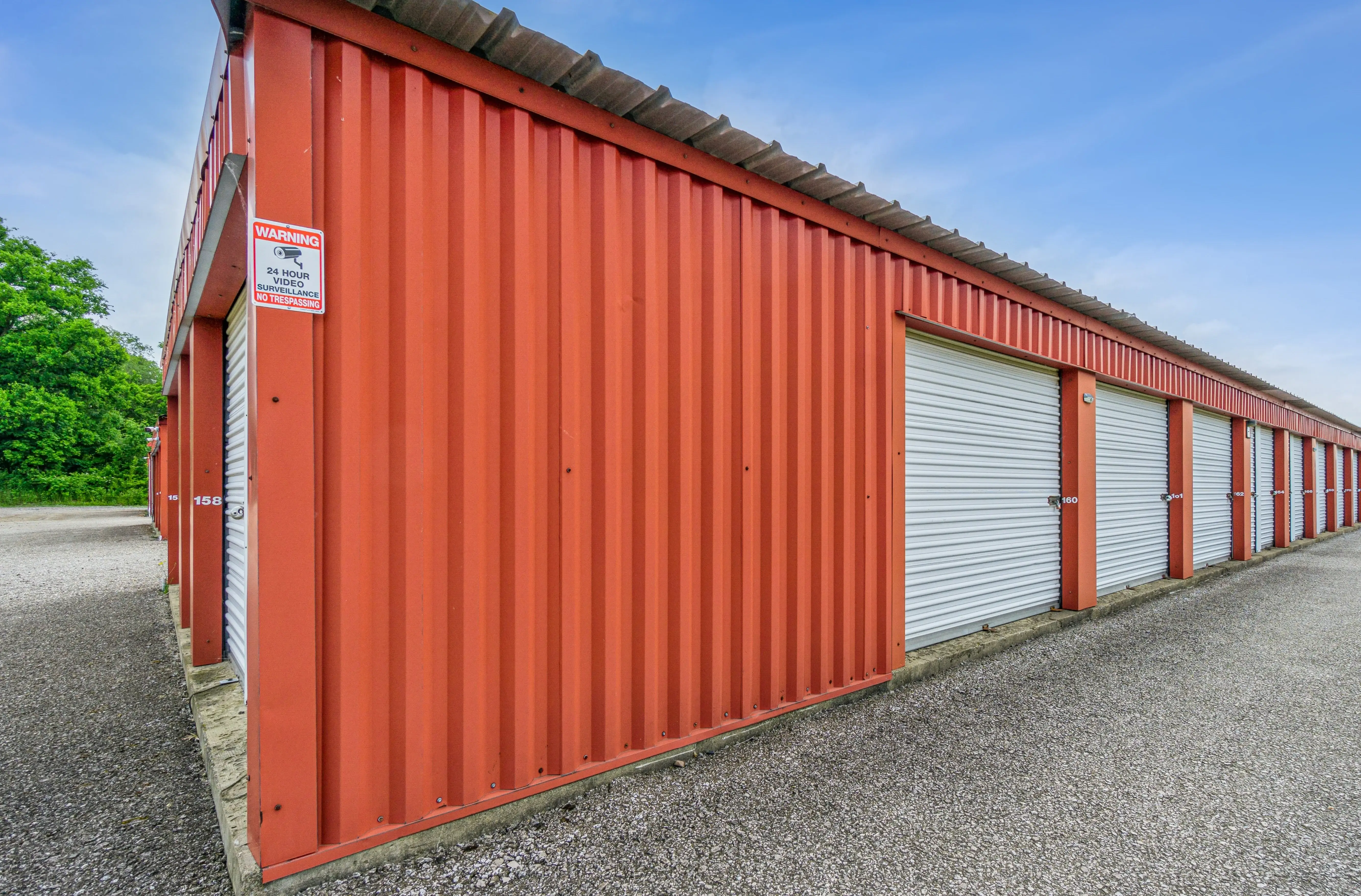 Close side-angle view of red drive up storage units with white roll up doors along a gravel surface in Fairview PA