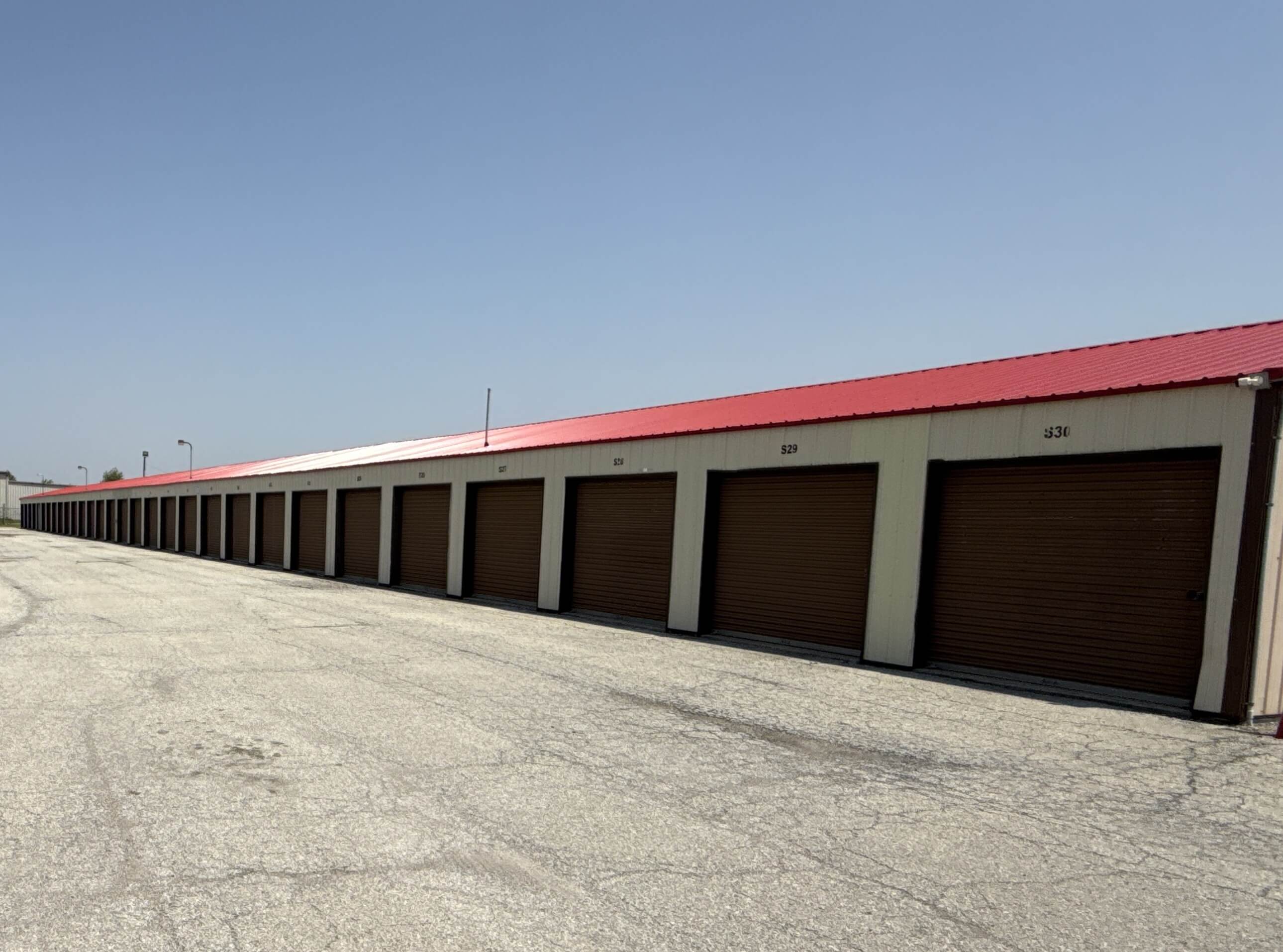 Row of drive up storage units with brown roll up doors and red roof at our Kokomo IN facility