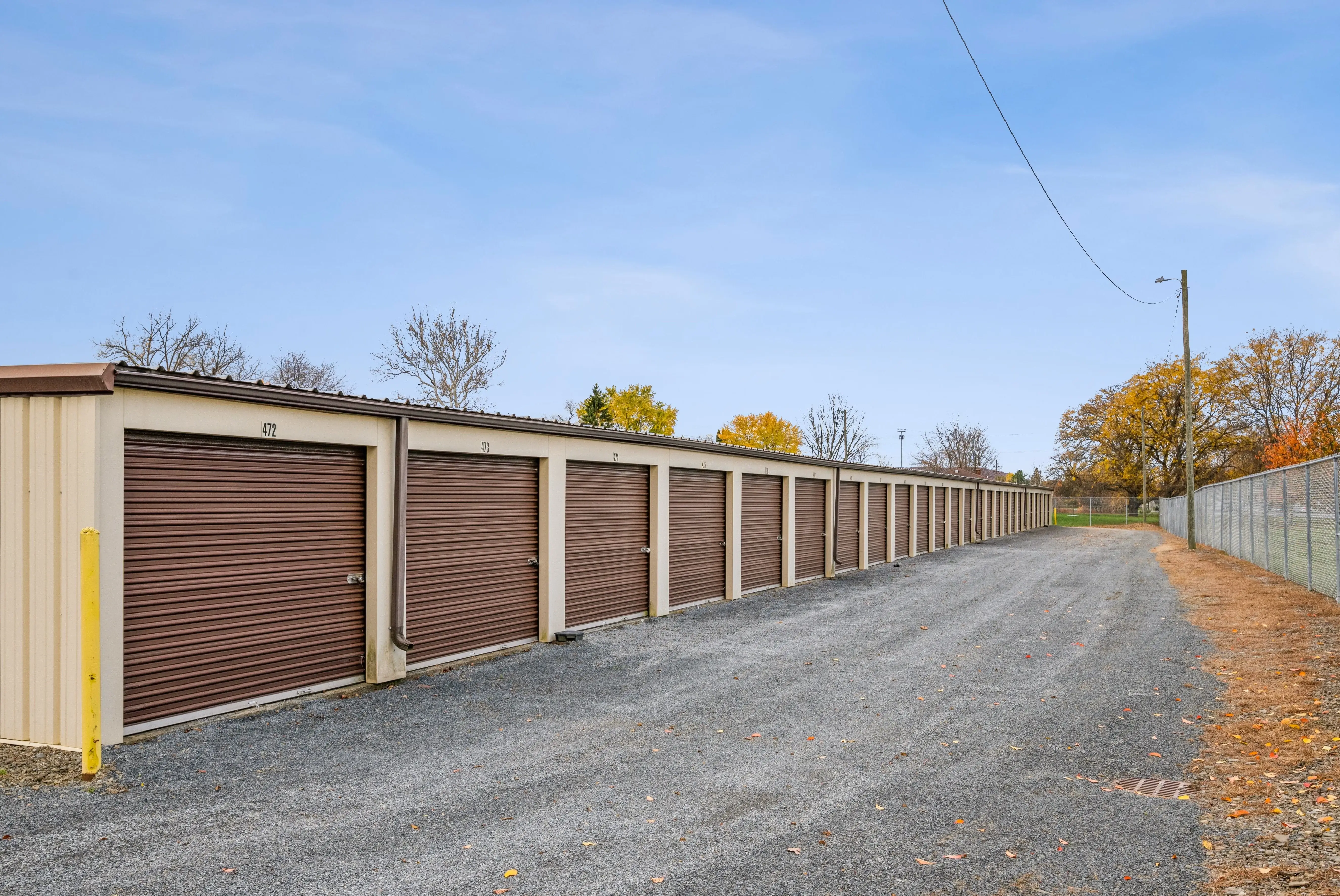 Row of drive up storage units with brown roll up doors along a gravel access lane in Horseheads NY