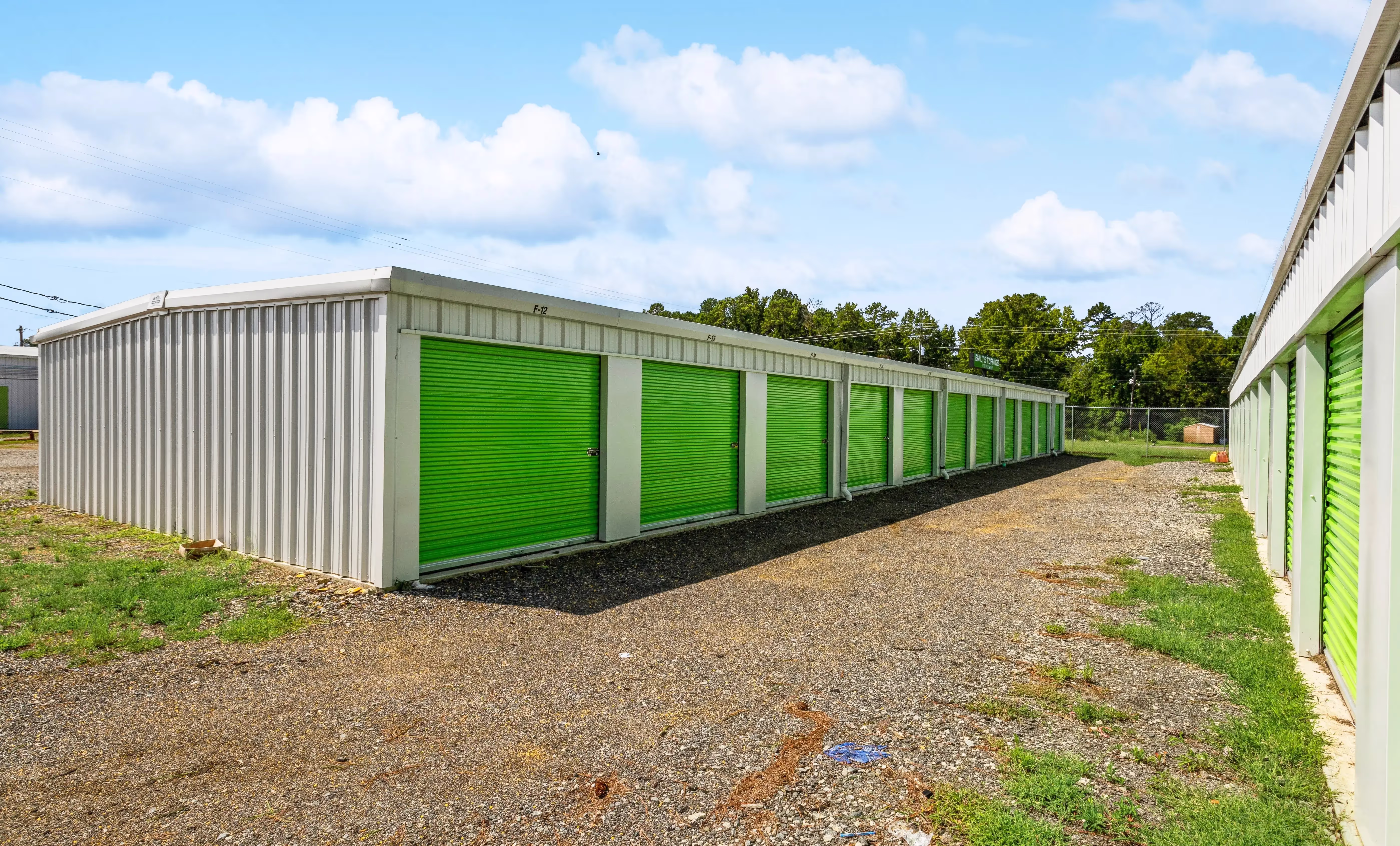 Row of drive up storage units with green doors on gravel driveway in Milledgeville GA