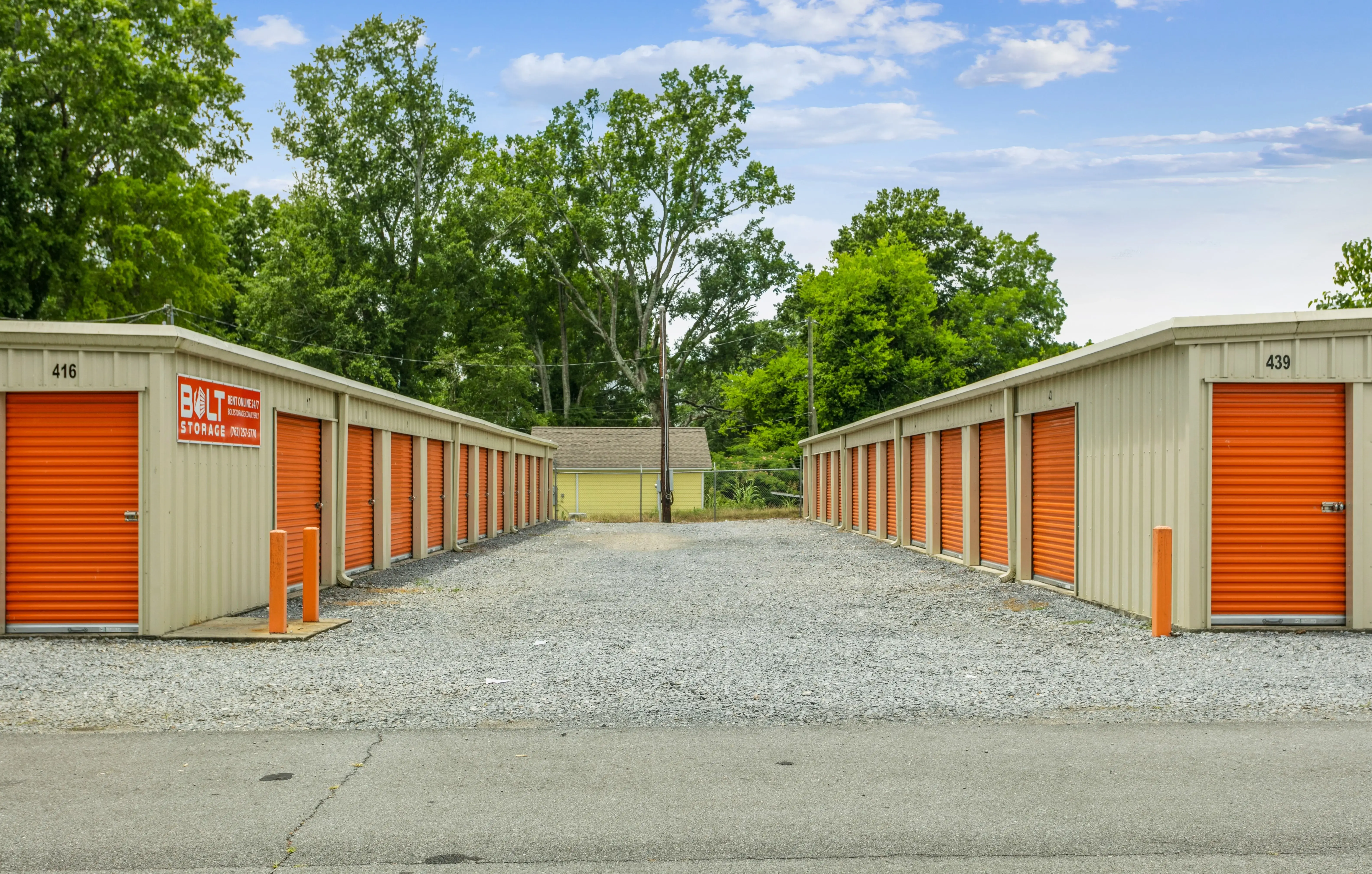 Drive up storage buildings with orange doors and gravel access lanes in Lyerly GA