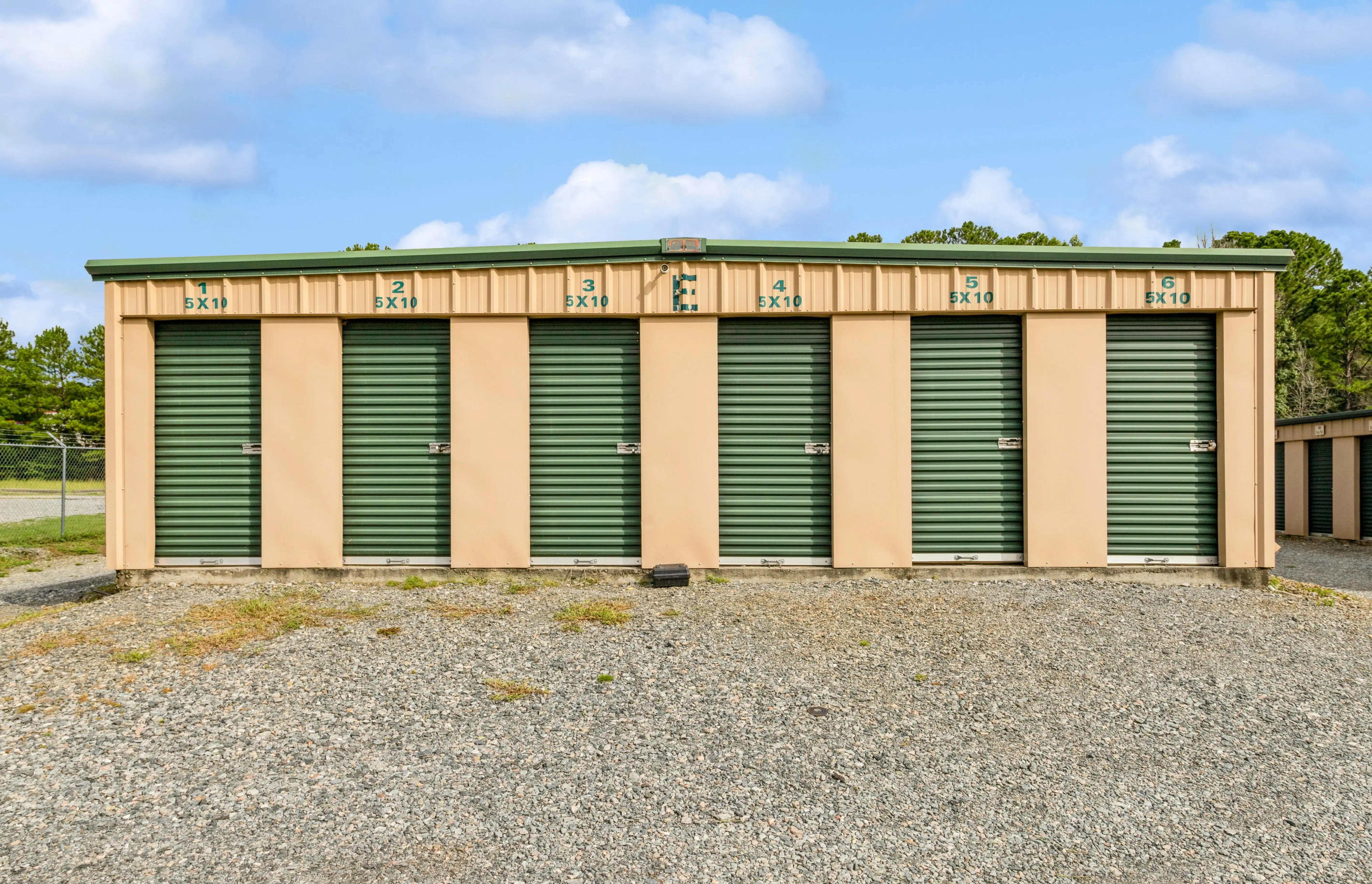 Exterior view of drive up storage units with green roll up doors on gravel driveway in Milledgeville GA