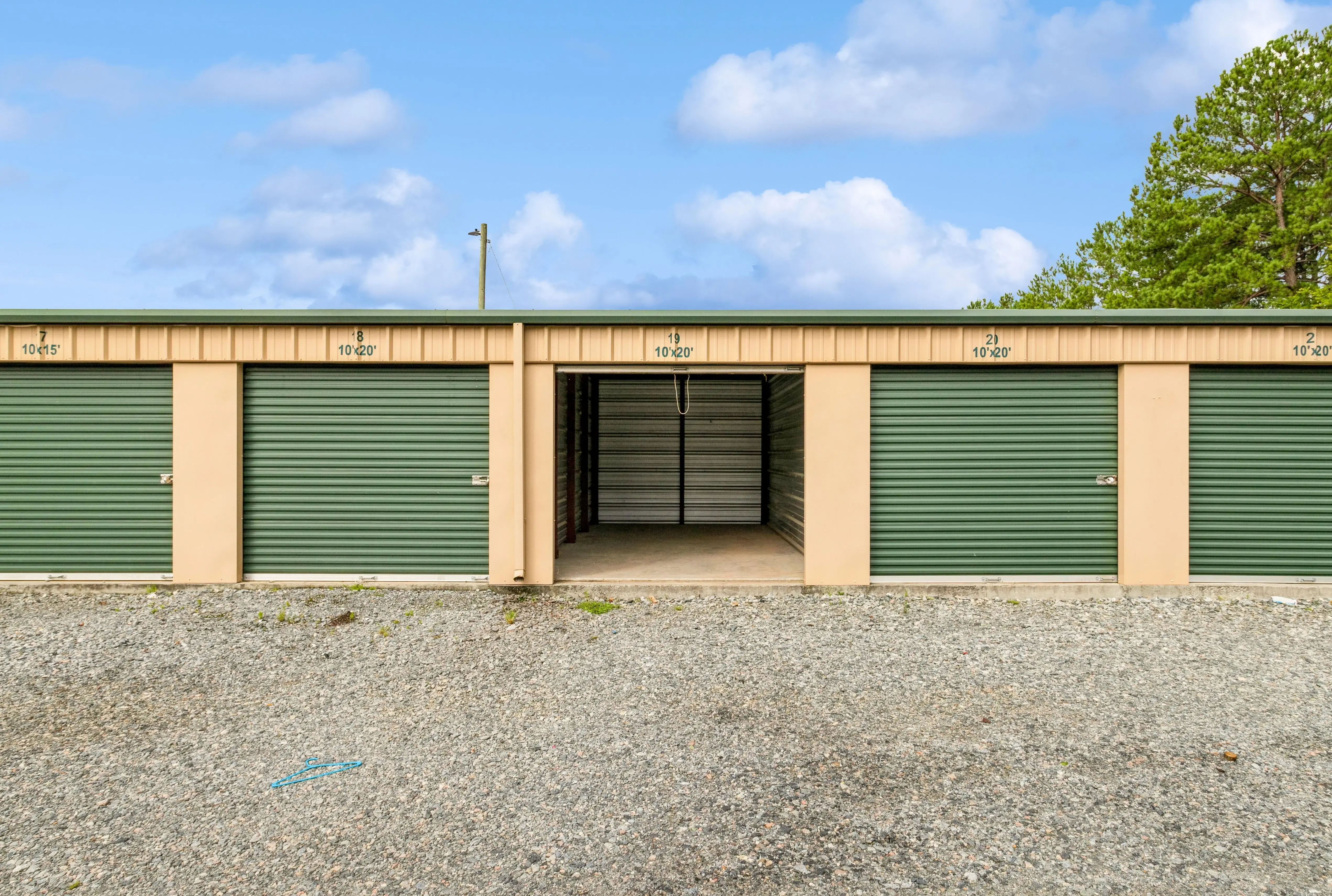 Drive up storage buildings with green roll up doors and gravel access lane in Milledgeville GA