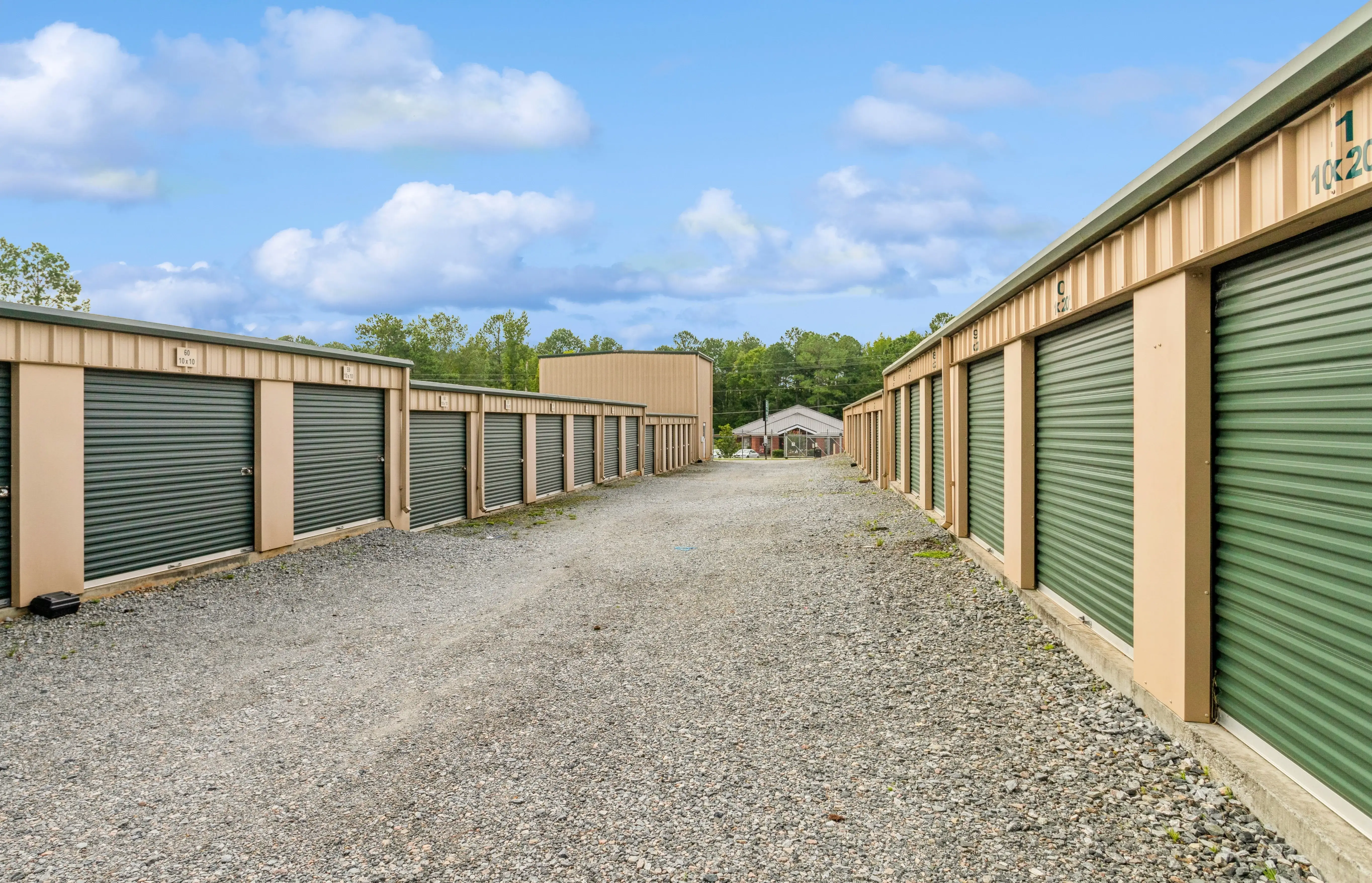 Angled view of drive up storage units with green doors along gravel driveway at our Milledgeville GA facility
