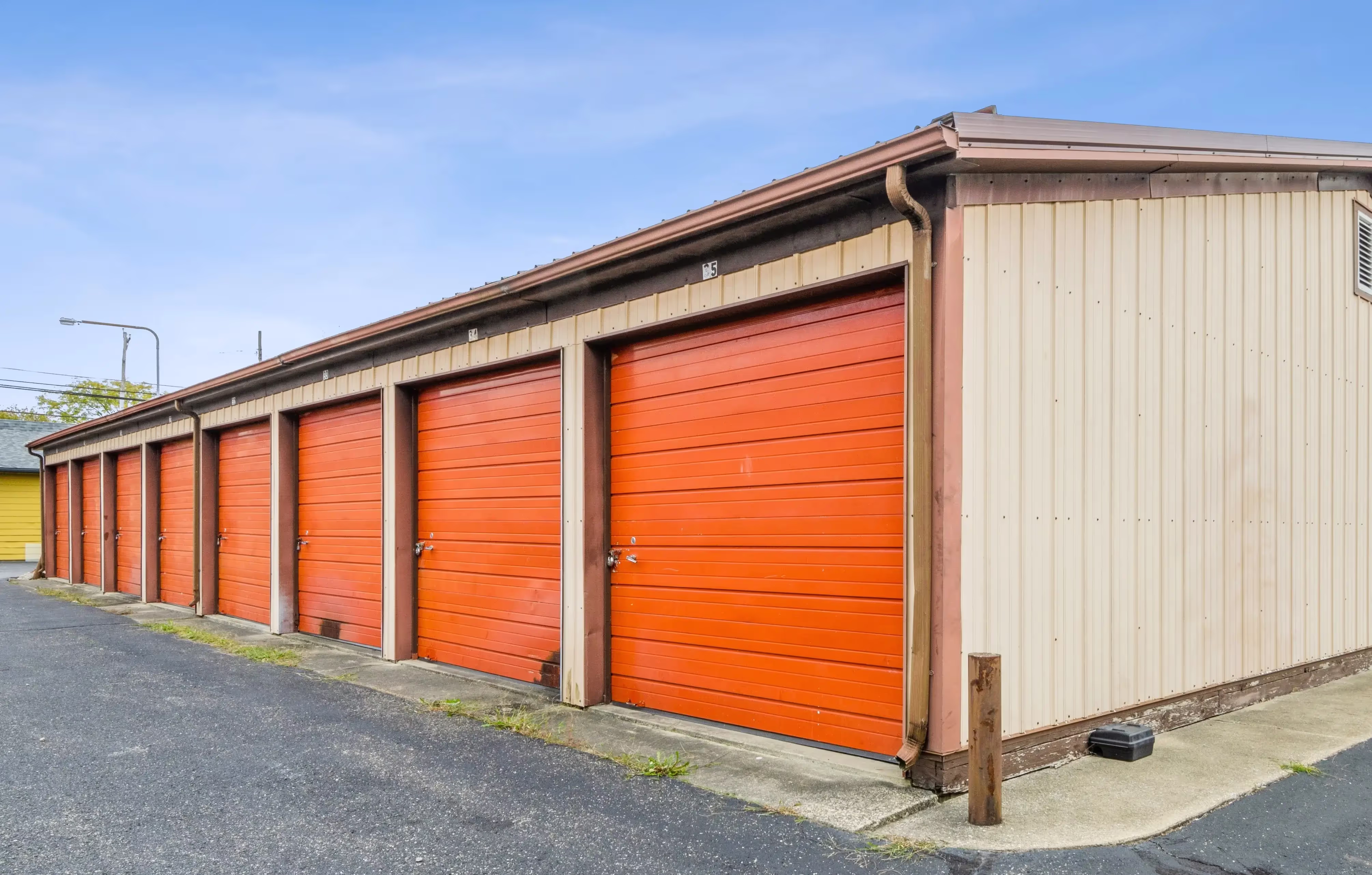 Row of drive up storage units with orange roll up doors along paved access lane in Peru IN