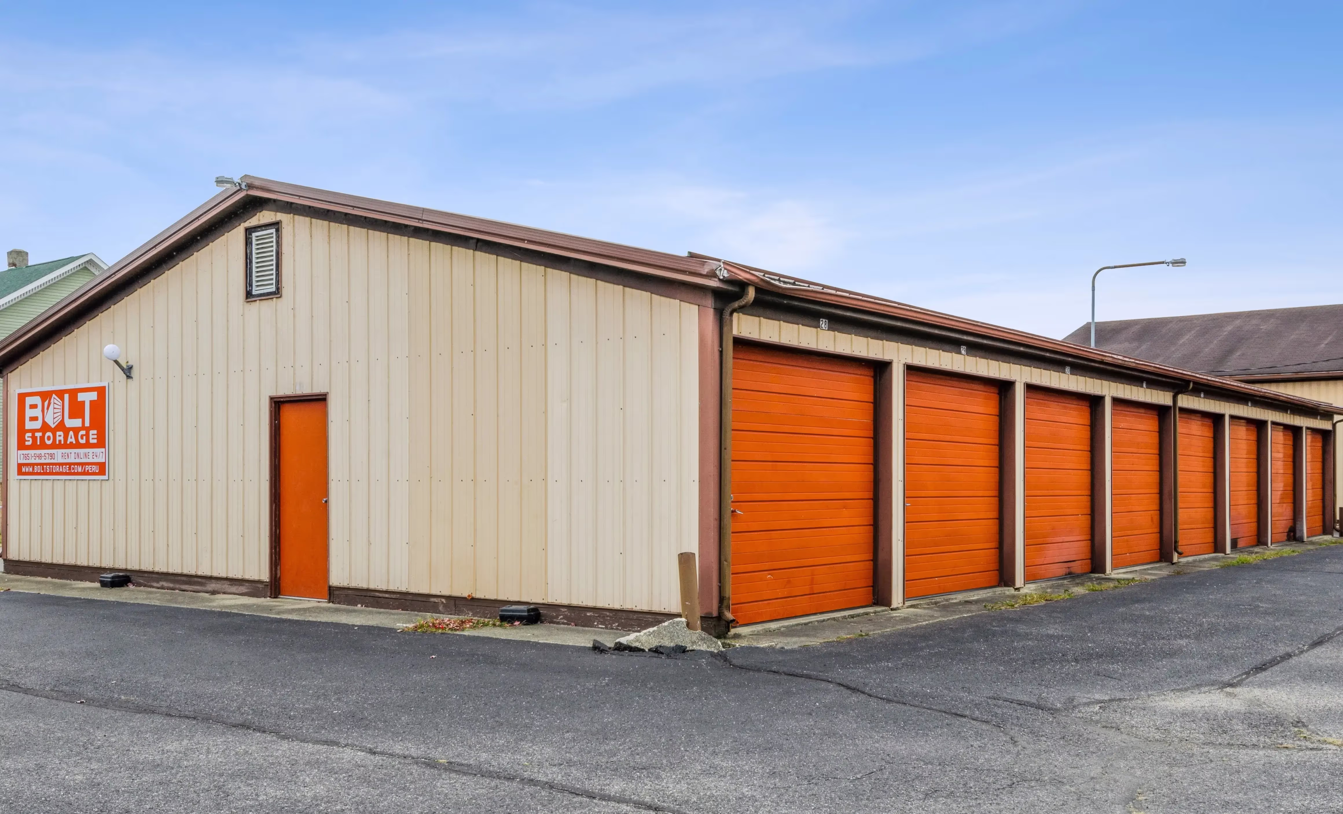 Angled view of drive up storage buildings with orange doors and paved driveway in Peru IN