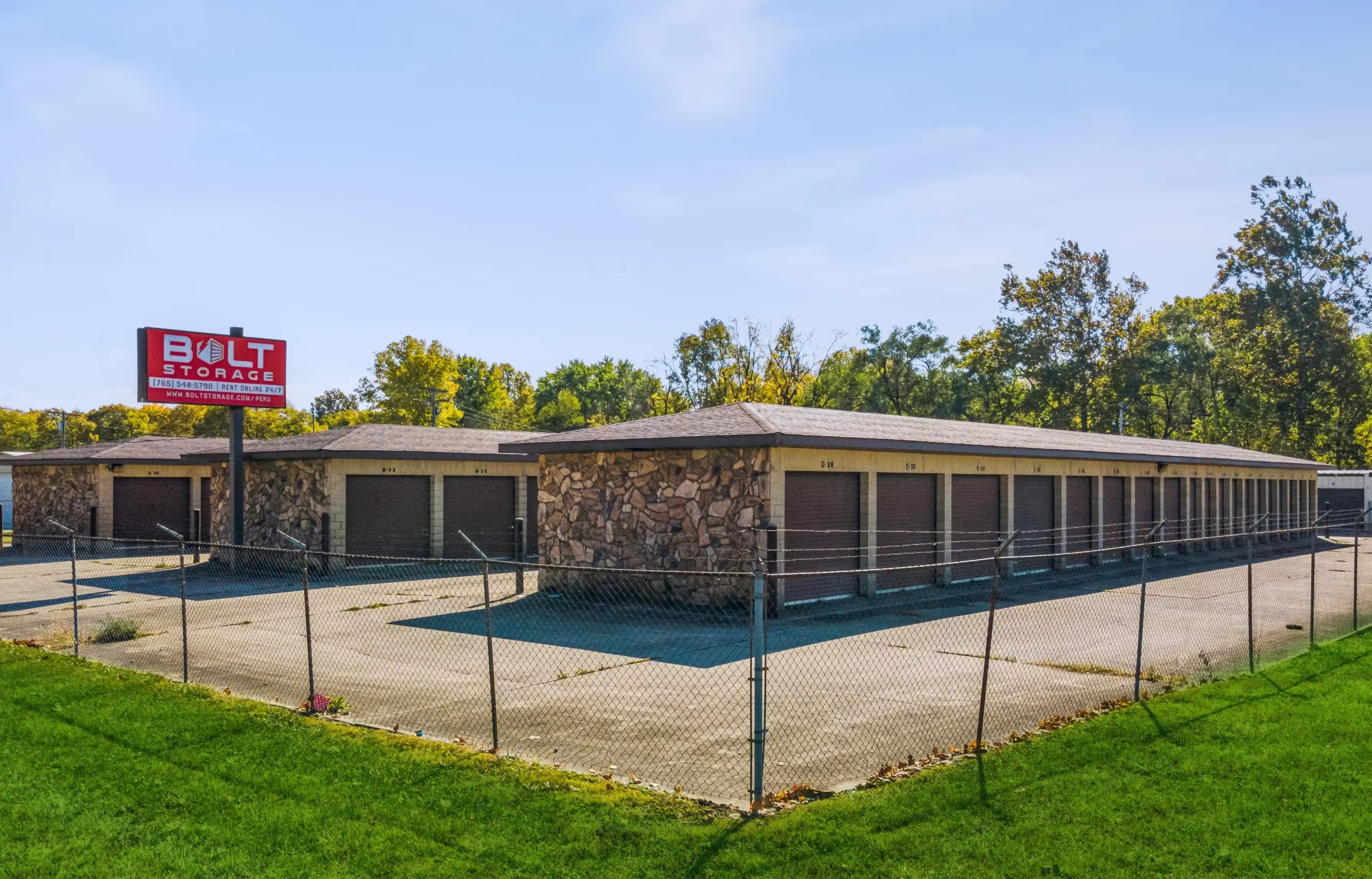View from the outside of a fenced self storage facility, and a red Bolt Storage sign