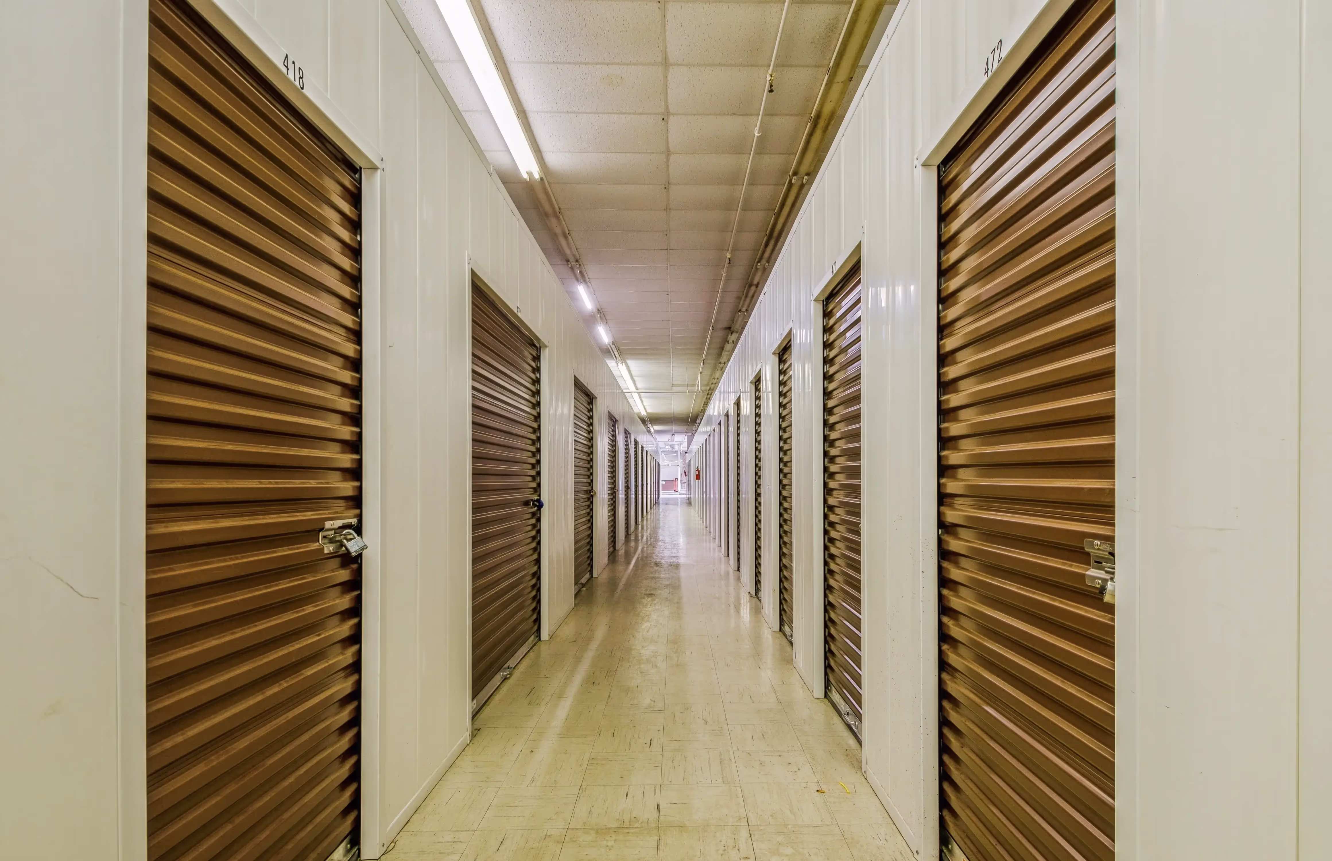 Deep interior hallway lined with brown doors and bright overhead lights inside our Peru IN storage facility