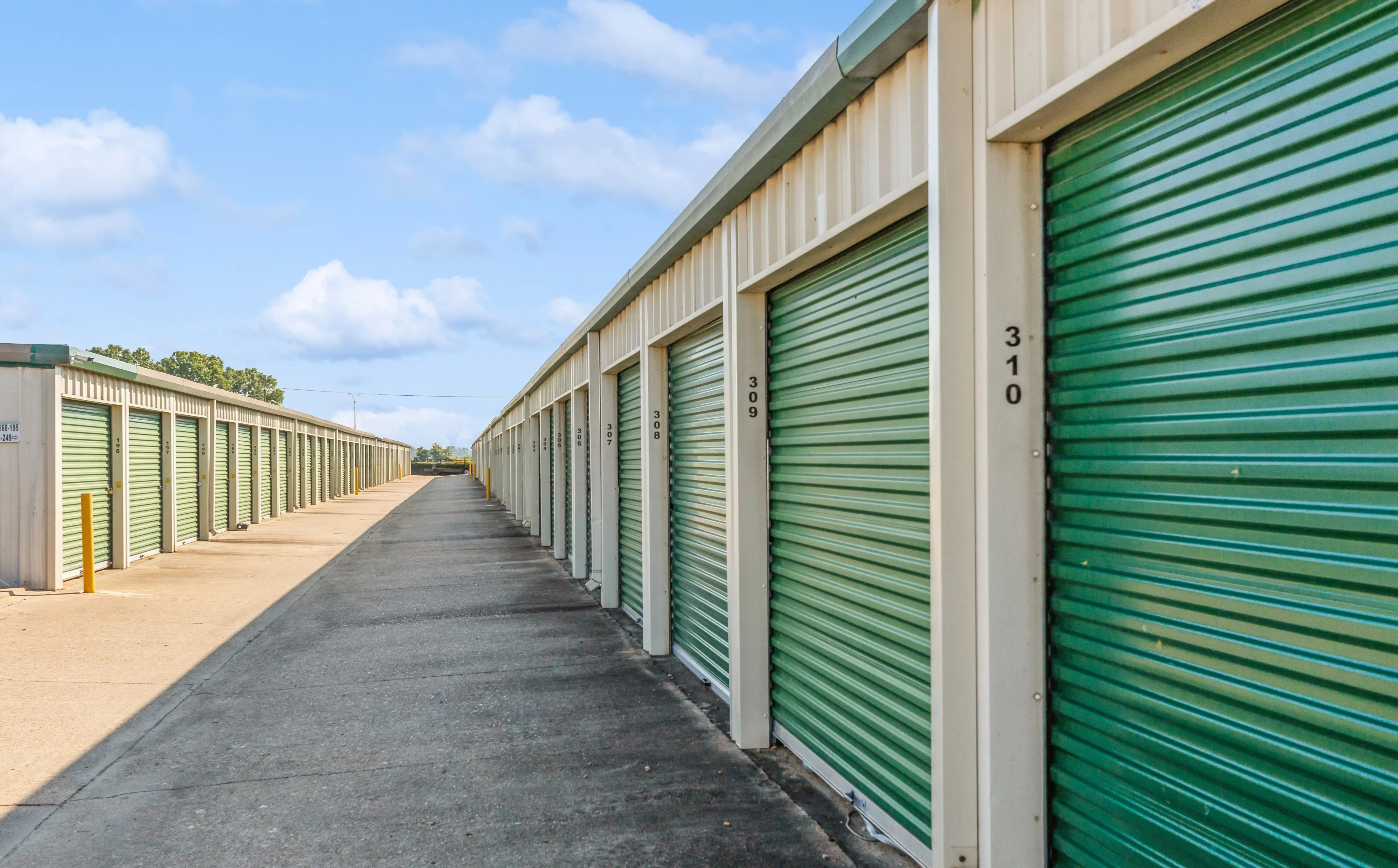 Row of drive up storage units with green roll up doors along paved access lane in Robinsonville MS