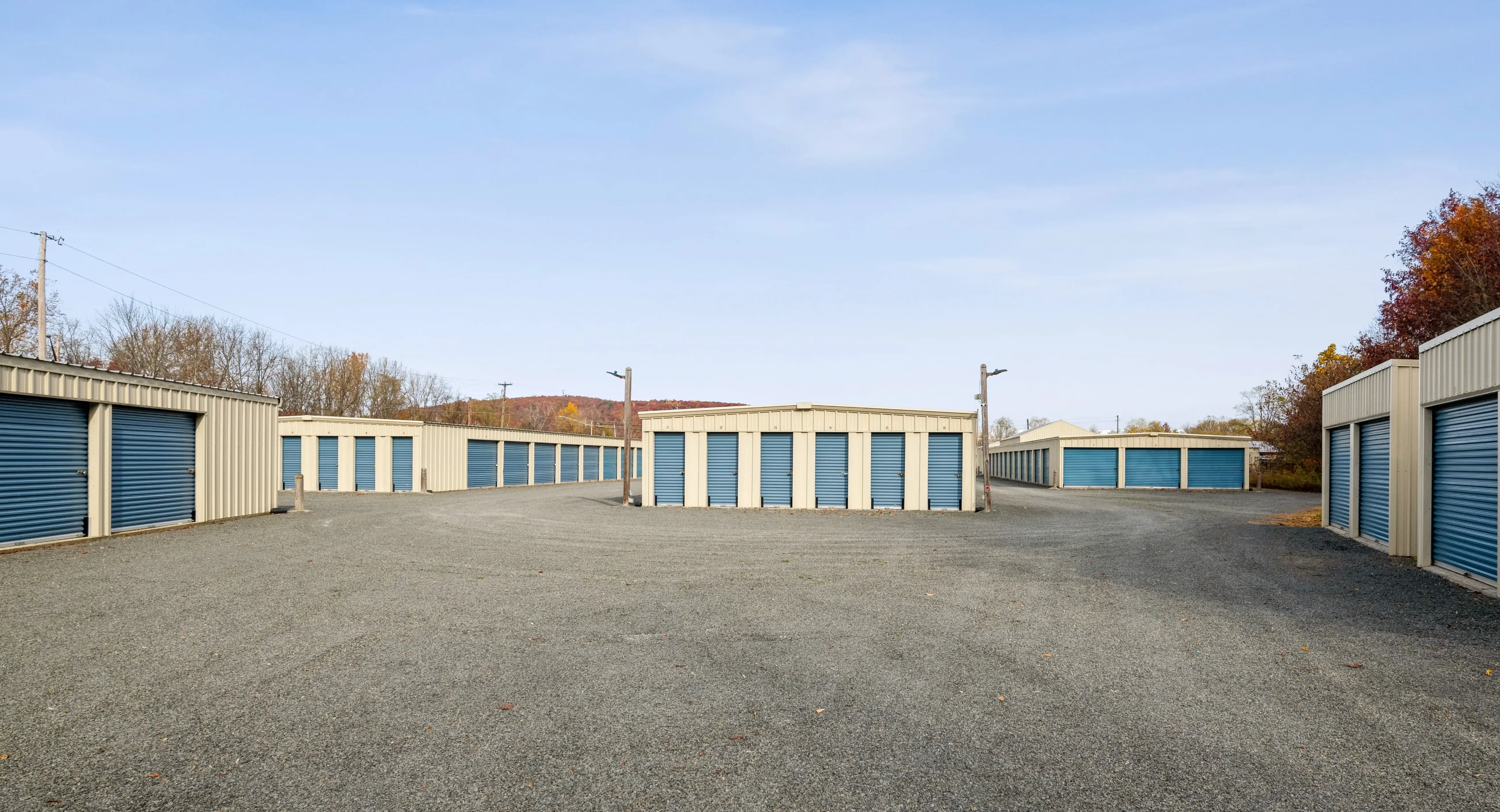 Row of drive up storage units with blue doors and gravel driveway in Elmira NY
